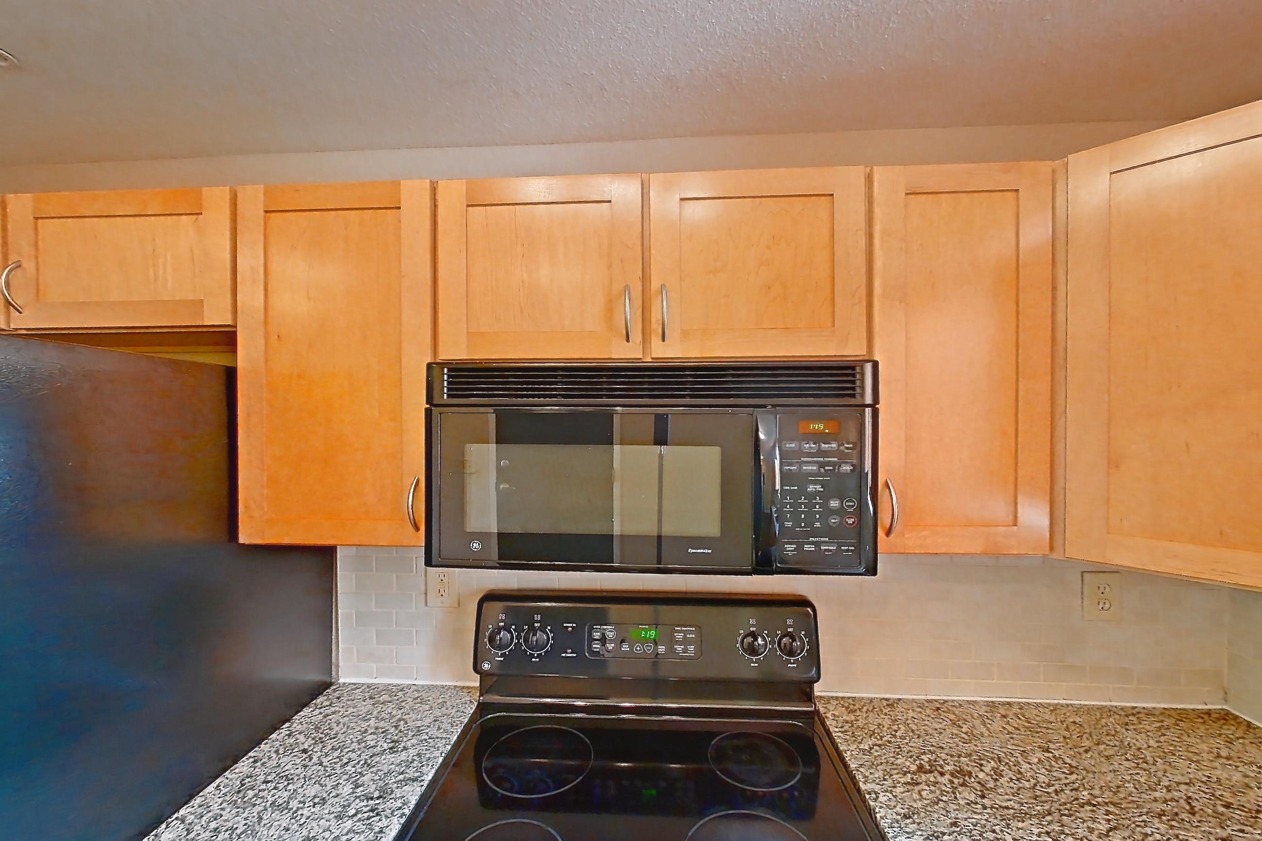 Kitchen with black appliances, dark wood-finish flooring, dishwasher, electric range, light stone countertops, microwave, oven/range, and refrigerator, Apartment A-464-2A at Cortland Belmar