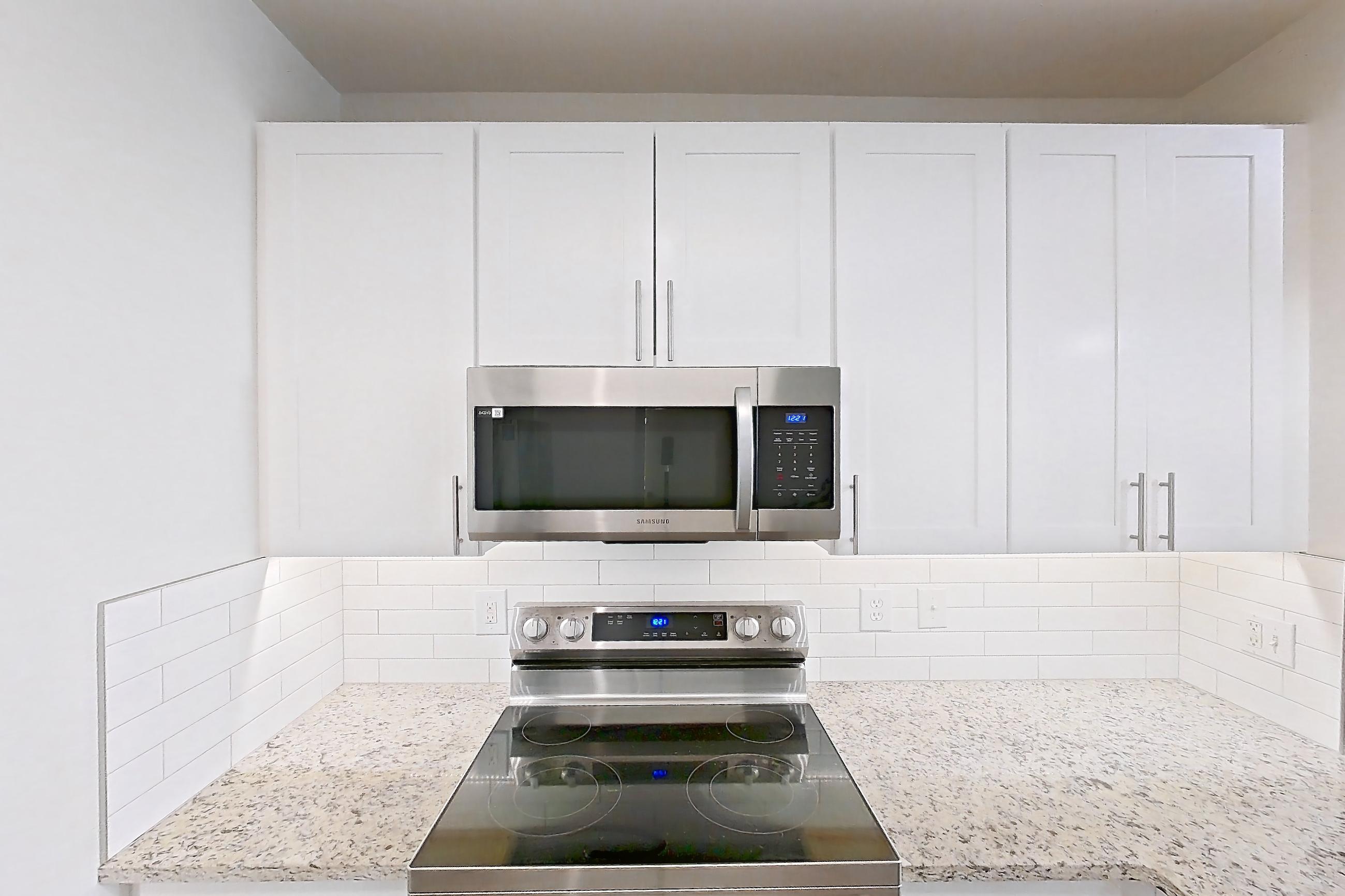 Kitchen with dishwasher, electric range, light countertops, light stone countertops, light wood-finish flooring, microwave, oven/range, refrigerator, and stainless steel appliances, Apartment C-424 at Cortland Belmar