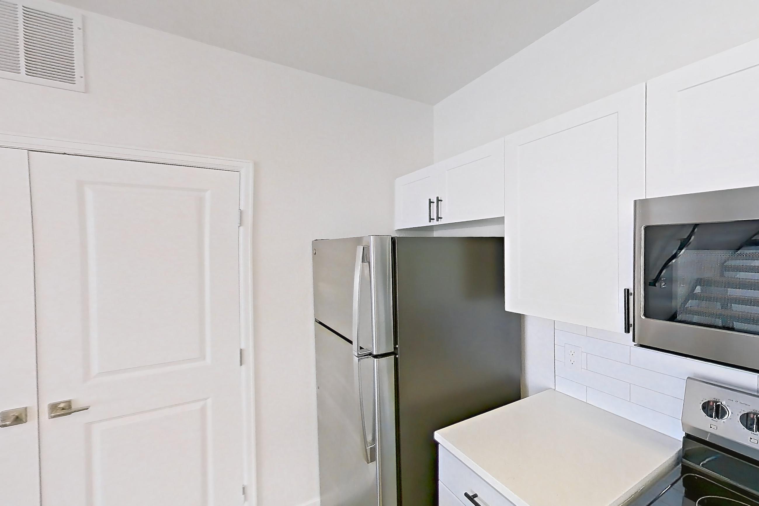 Kitchen with dishwasher, electric range, light countertops, light stone countertops, light wood-finish flooring, microwave, oven/range, refrigerator, and stainless steel appliances, Apartment C-440 at Cortland Belmar