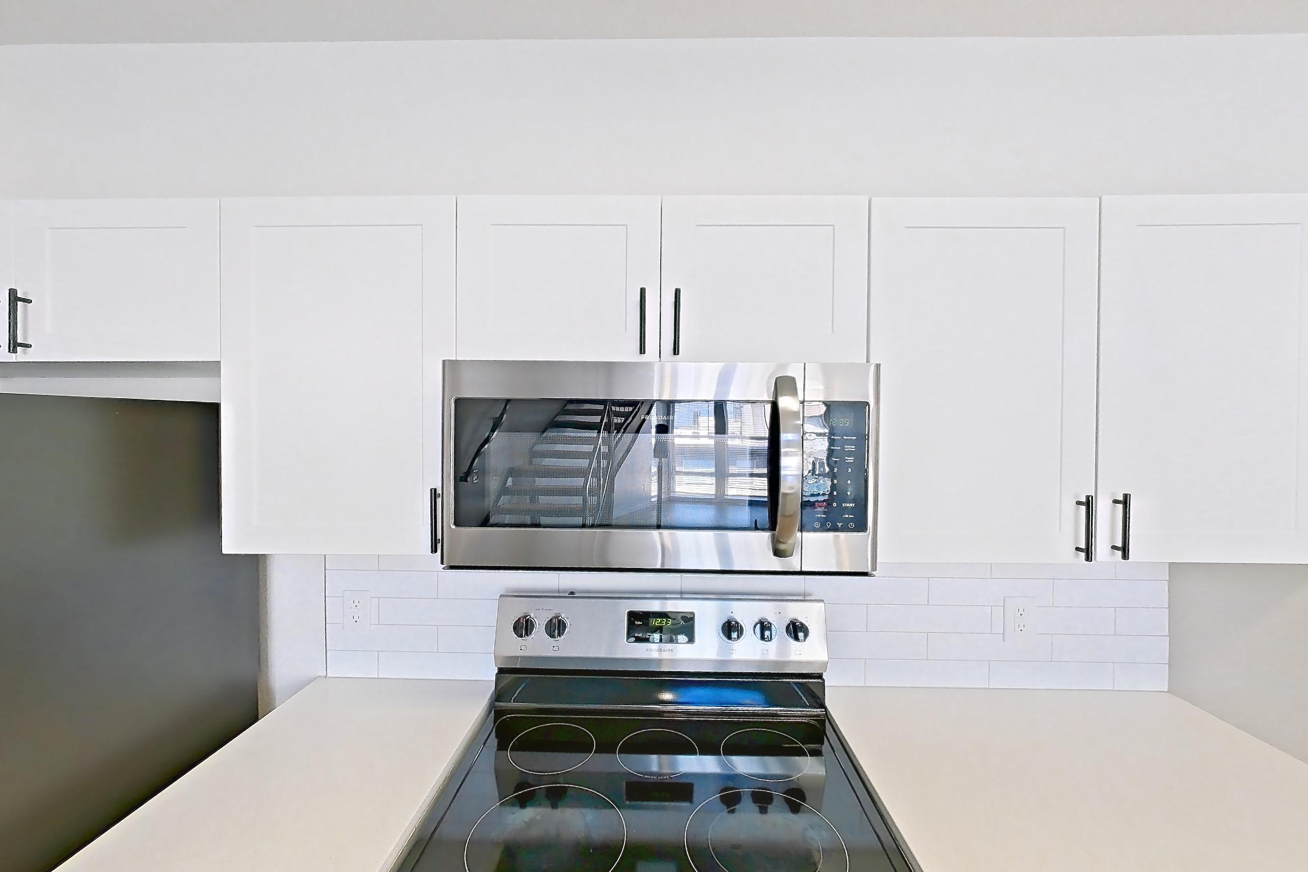 Kitchen with dishwasher, electric range, light countertops, light stone countertops, light wood-finish flooring, microwave, oven/range, refrigerator, and stainless steel appliances, Apartment C-440 at Cortland Belmar