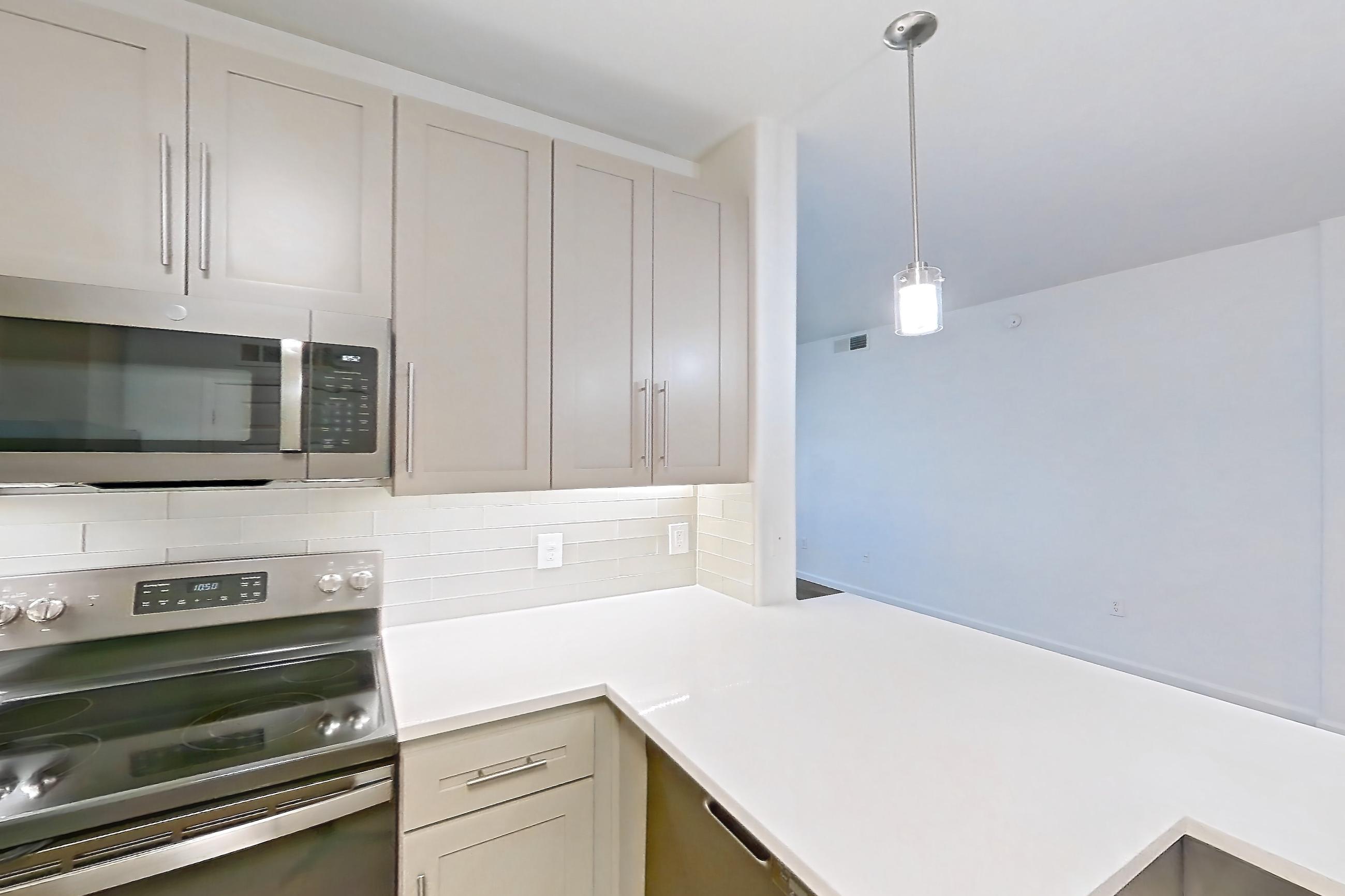 Kitchen with electric range, kitchen island, light countertops, light wood-finish flooring, microwave, oven/range, refrigerator, and stainless steel appliances, Apartment 1066 at Cortland South Mountain