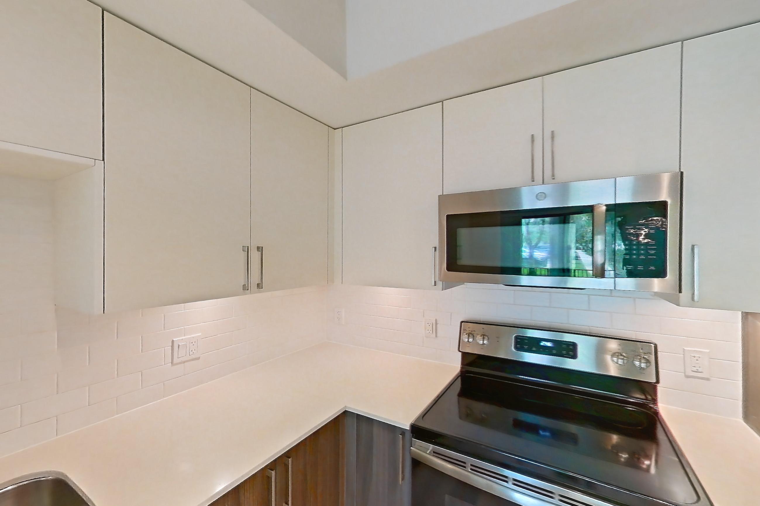 Kitchen with dishwasher, electric range, light countertops, light stone countertops, light wood-finish flooring, microwave, oven/range, refrigerator, and stainless steel appliances, Apartment 04-106 at Cortland South Kendall