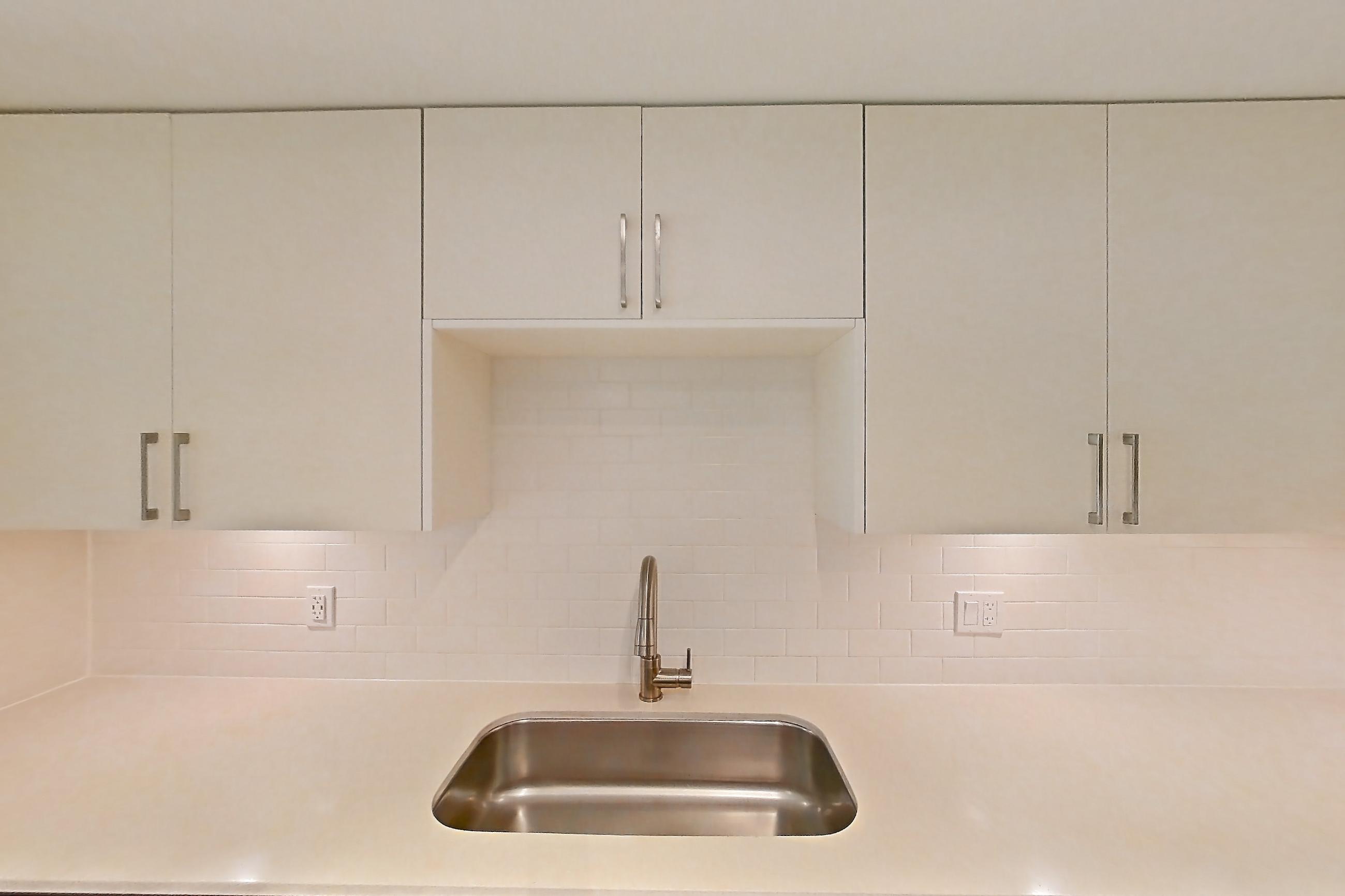 Kitchen with dishwasher, electric range, light countertops, light stone countertops, light wood-finish flooring, microwave, oven/range, refrigerator, and stainless steel appliances, Apartment 04-106 at Cortland South Kendall