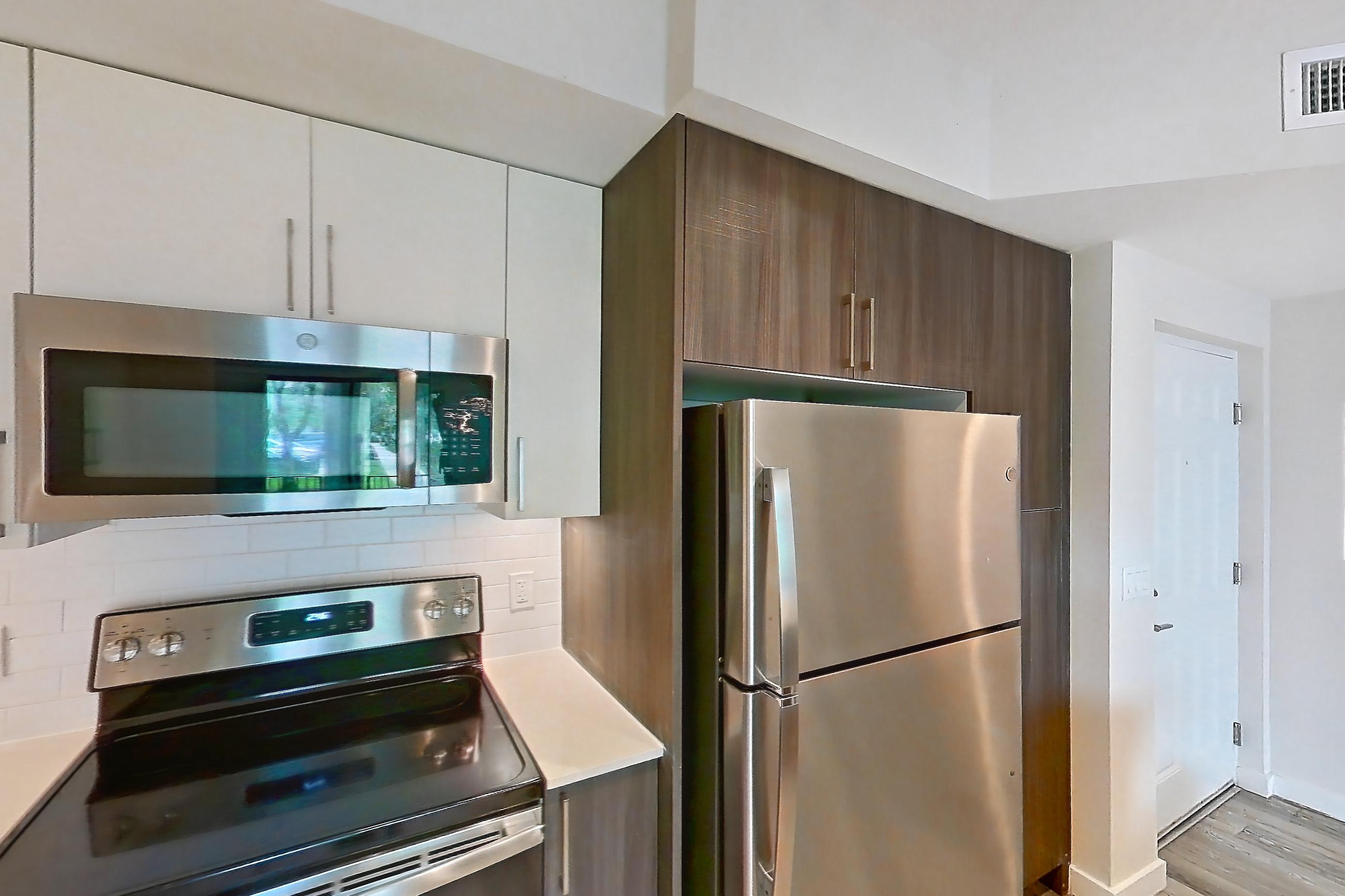 Kitchen with dishwasher, electric range, light countertops, light stone countertops, light wood-finish flooring, microwave, oven/range, refrigerator, and stainless steel appliances, Apartment 04-106 at Cortland South Kendall