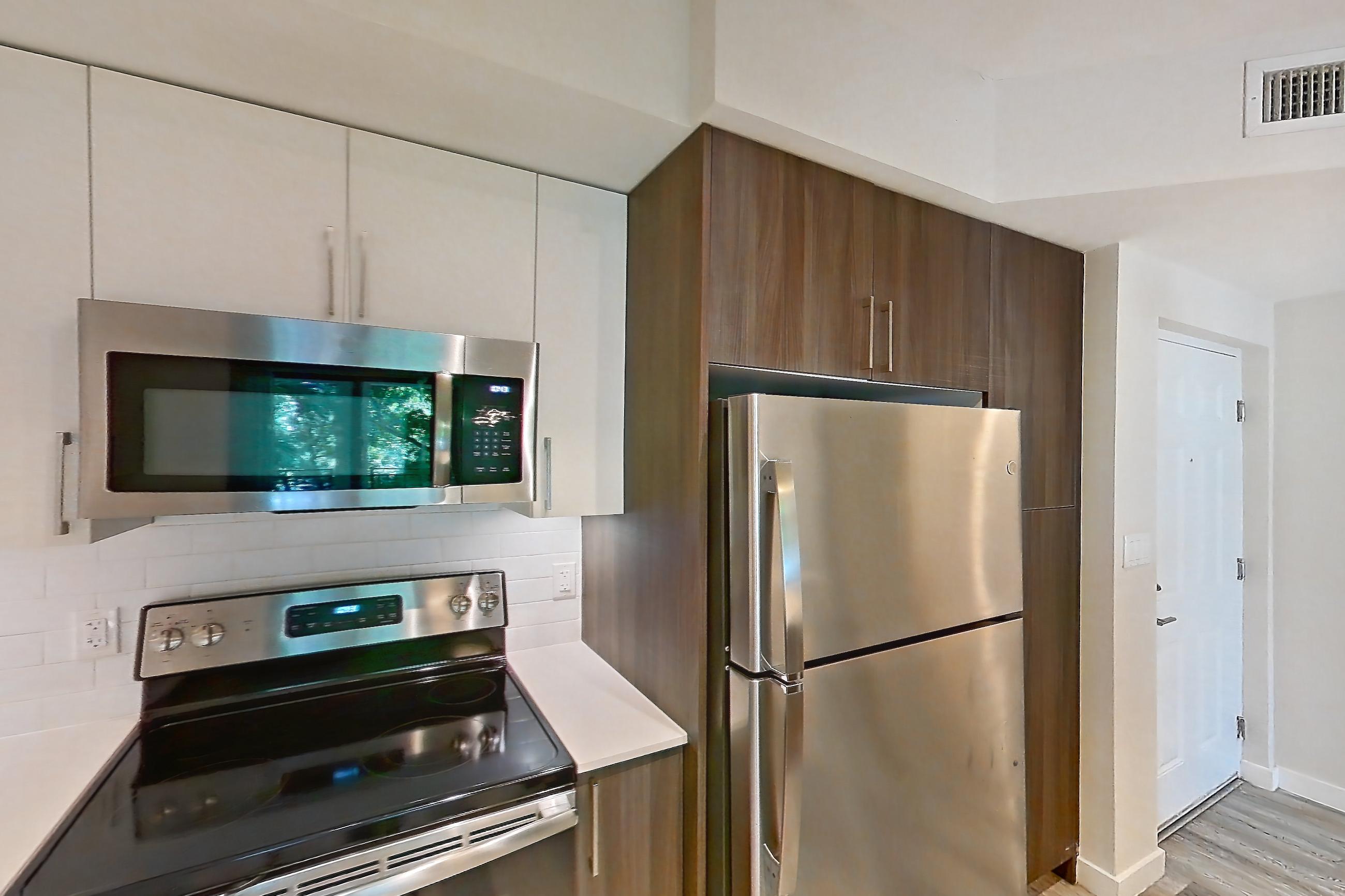 Kitchen with dishwasher, electric range, light countertops, light stone countertops, light wood-finish flooring, microwave, oven/range, refrigerator, and stainless steel appliances, Apartment 04-206 at Cortland South Kendall