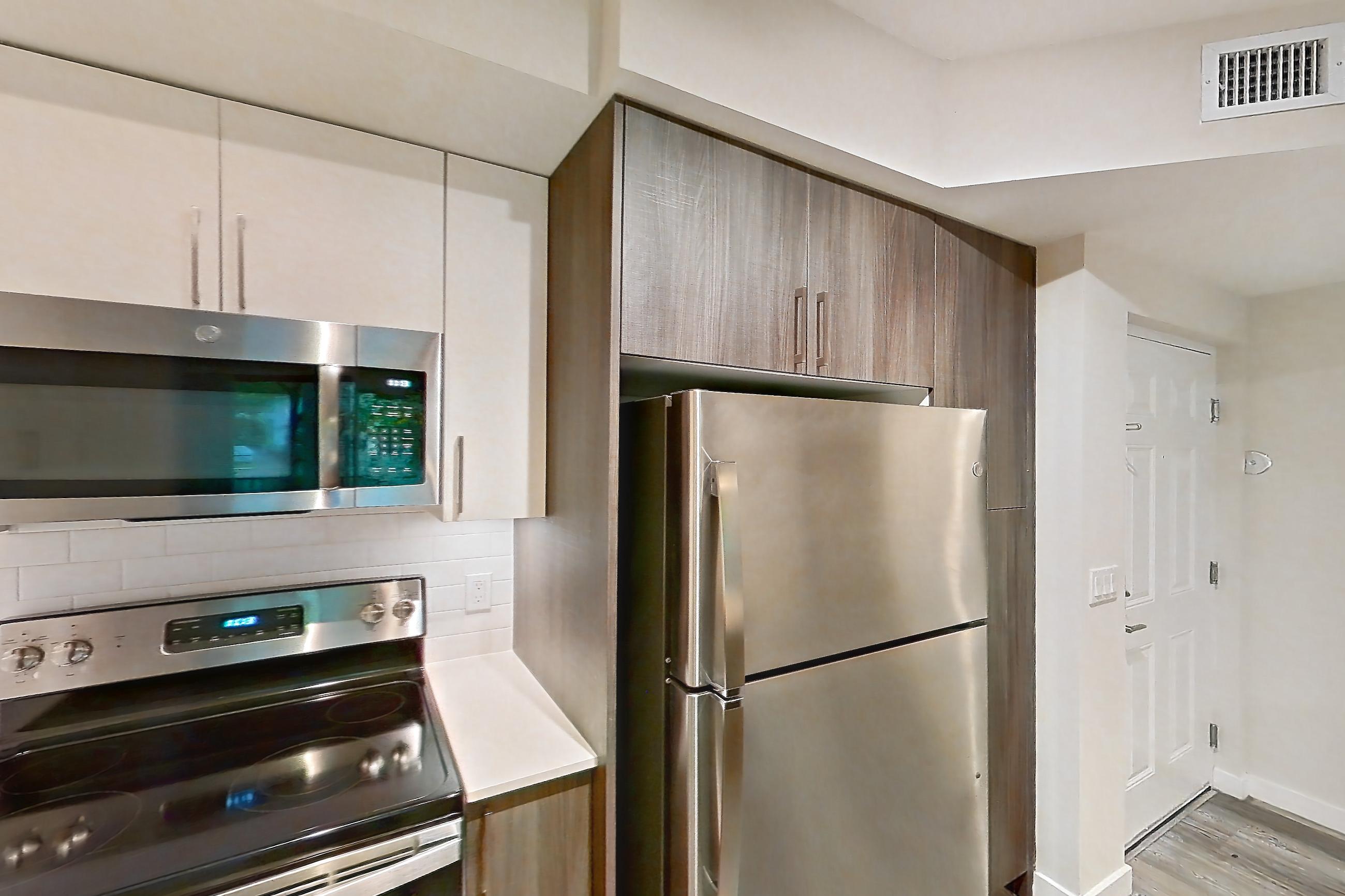 Kitchen with dishwasher, electric range, light countertops, light stone countertops, light wood-finish flooring, microwave, oven/range, refrigerator, and stainless steel appliances, Apartment 09-107 at Cortland South Kendall