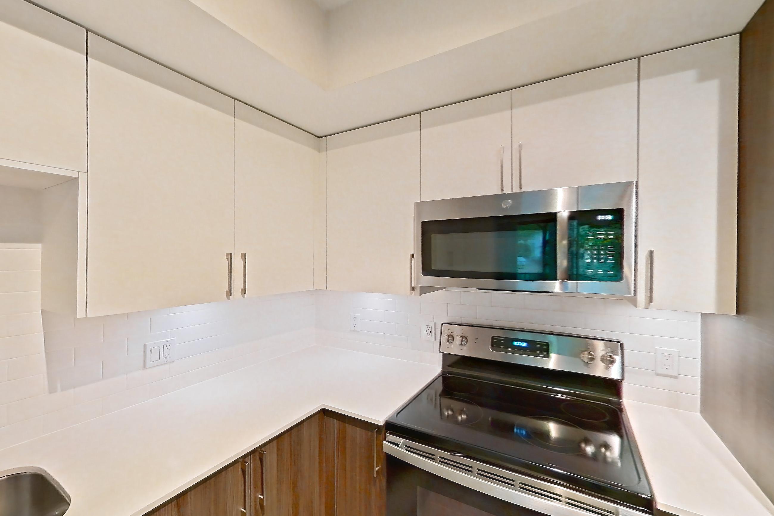 Kitchen with dishwasher, electric range, light countertops, light stone countertops, light wood-finish flooring, microwave, oven/range, refrigerator, and stainless steel appliances, Apartment 09-107 at Cortland South Kendall