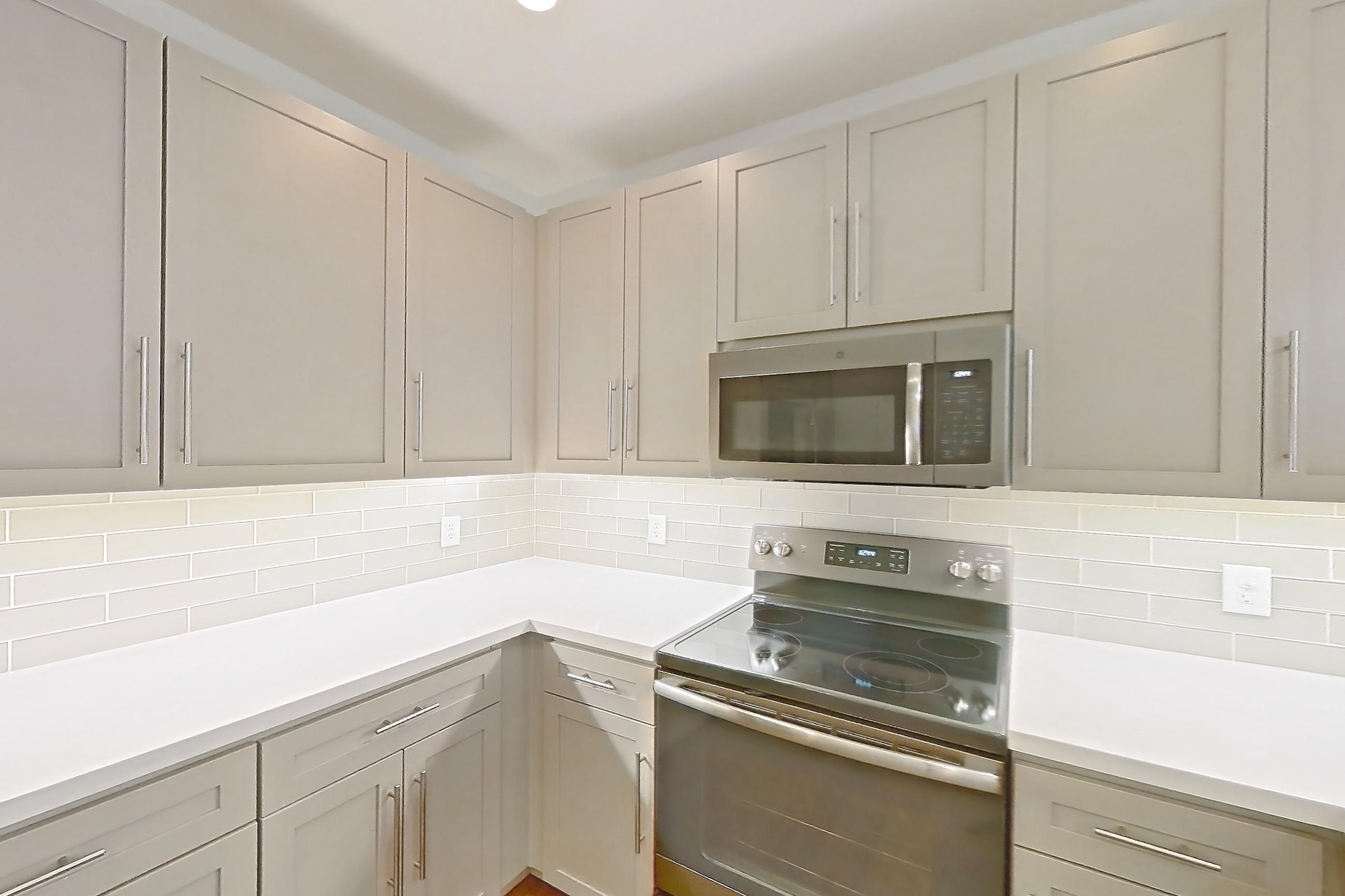 Kitchen with dark wood-finish flooring, dishwasher, electric range, light countertops, light stone countertops, light wood-finish flooring, microwave, oven/range, and stainless steel appliances, Apartment 3091 at Cortland South Mountain