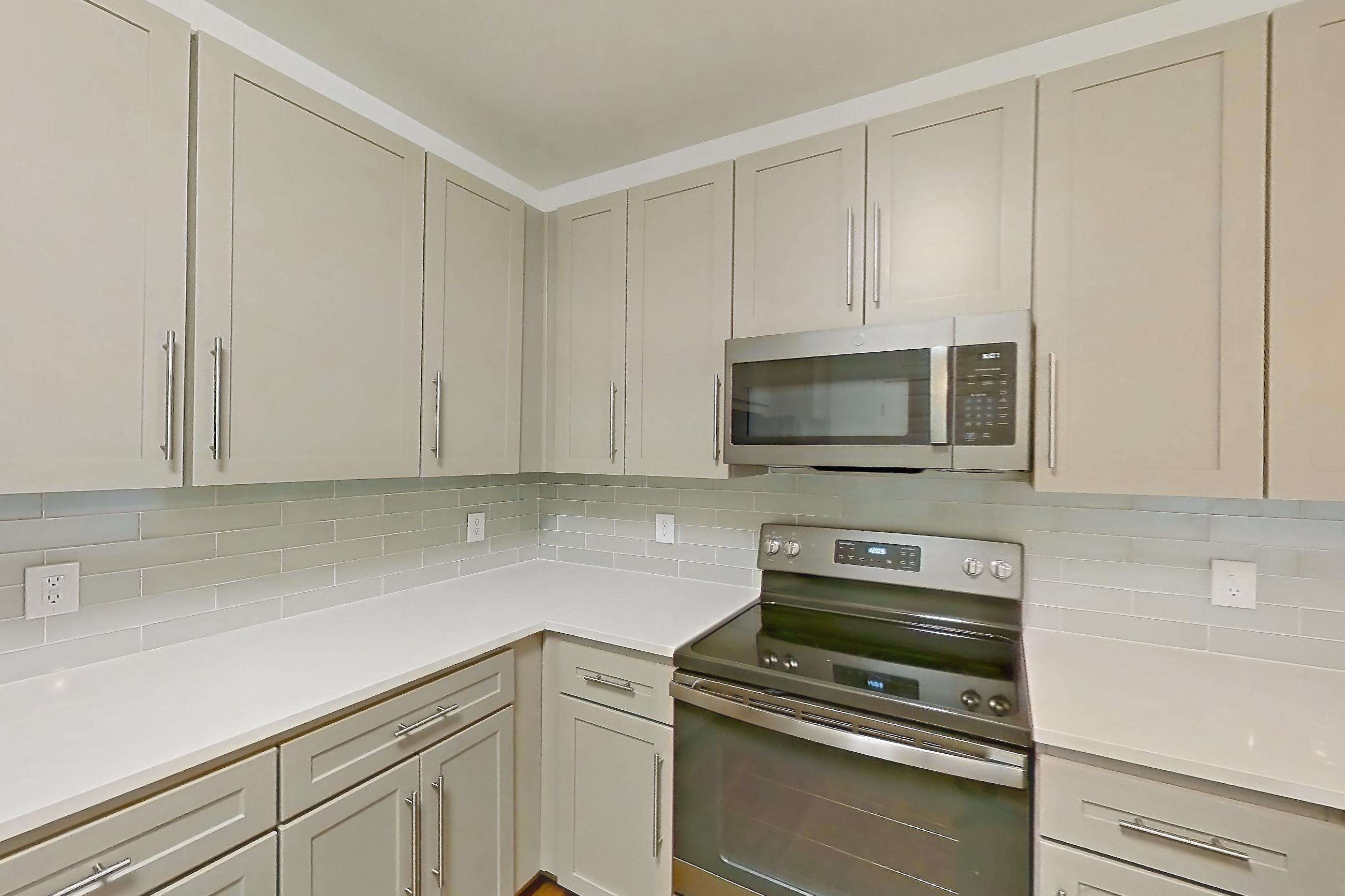 Kitchen with dark wood-finish flooring, dishwasher, electric range, kitchen island, light countertops, light stone countertops, light wood-finish flooring, microwave, oven/range, and stainless steel appliances, Apartment 3101 at Cortland South Mountain