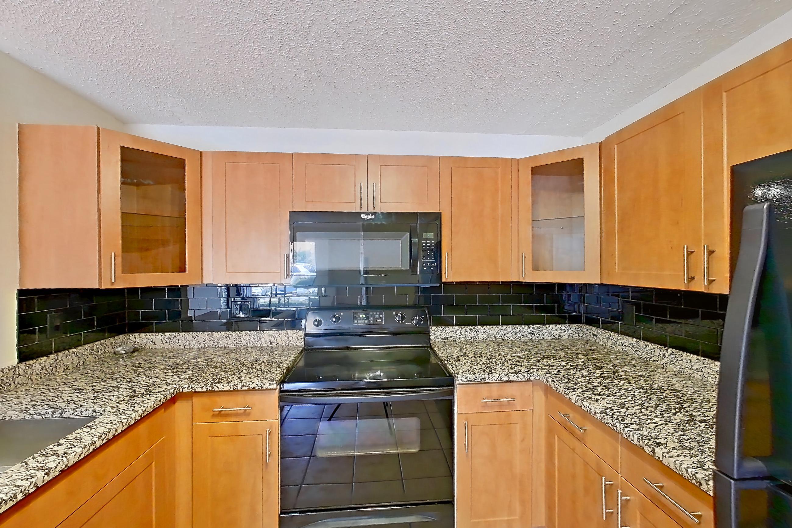 Kitchen with black appliances, dishwasher, electric range, light stone countertops, light tile flooring, microwave, oven/range, and refrigerator, Apartment 465442 at Cortland Bayport