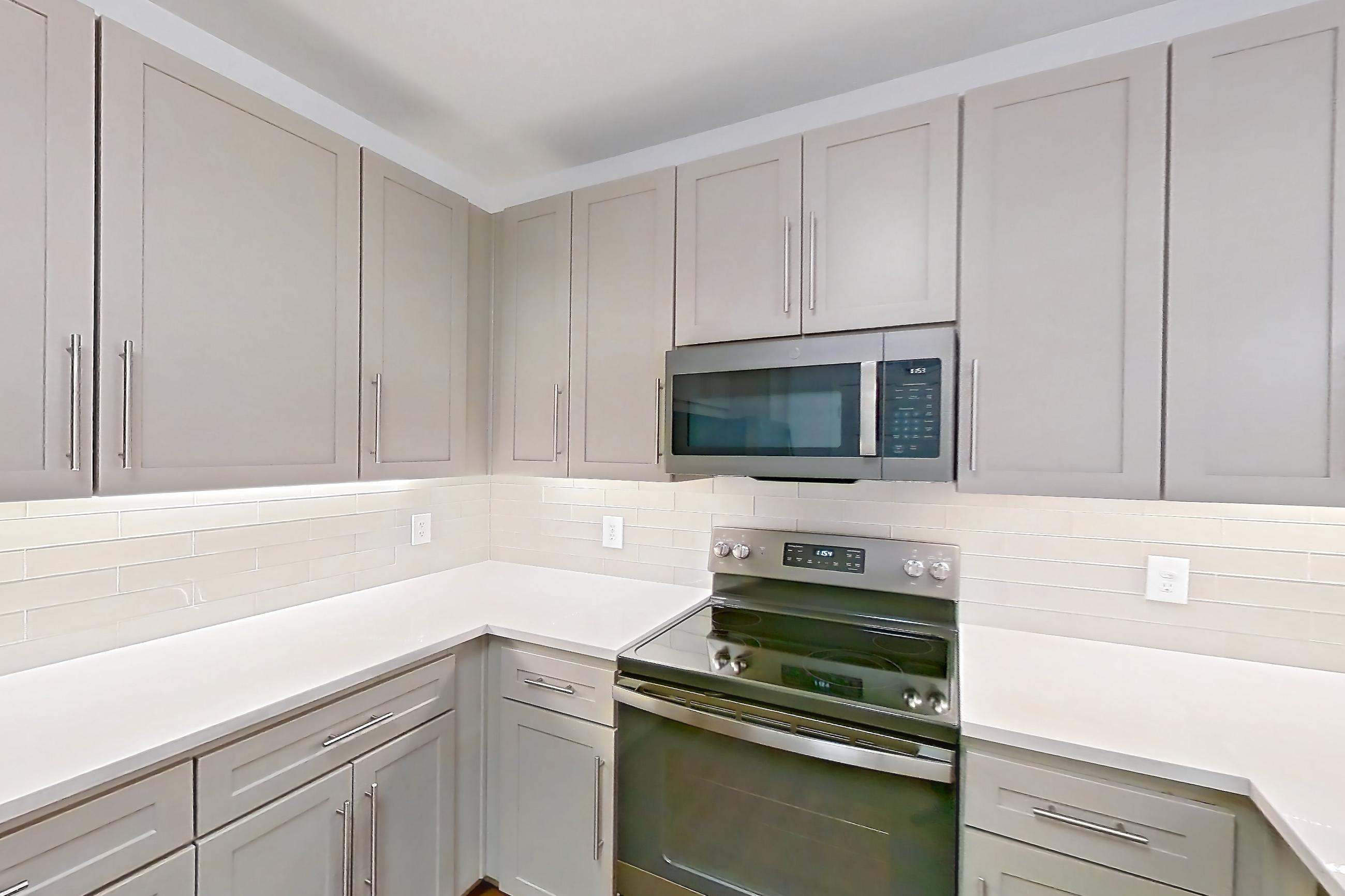 Kitchen with electric range, kitchen island, light countertops, light wood-finish flooring, microwave, oven/range, and stainless steel appliances, Apartment 3113 at Cortland South Mountain