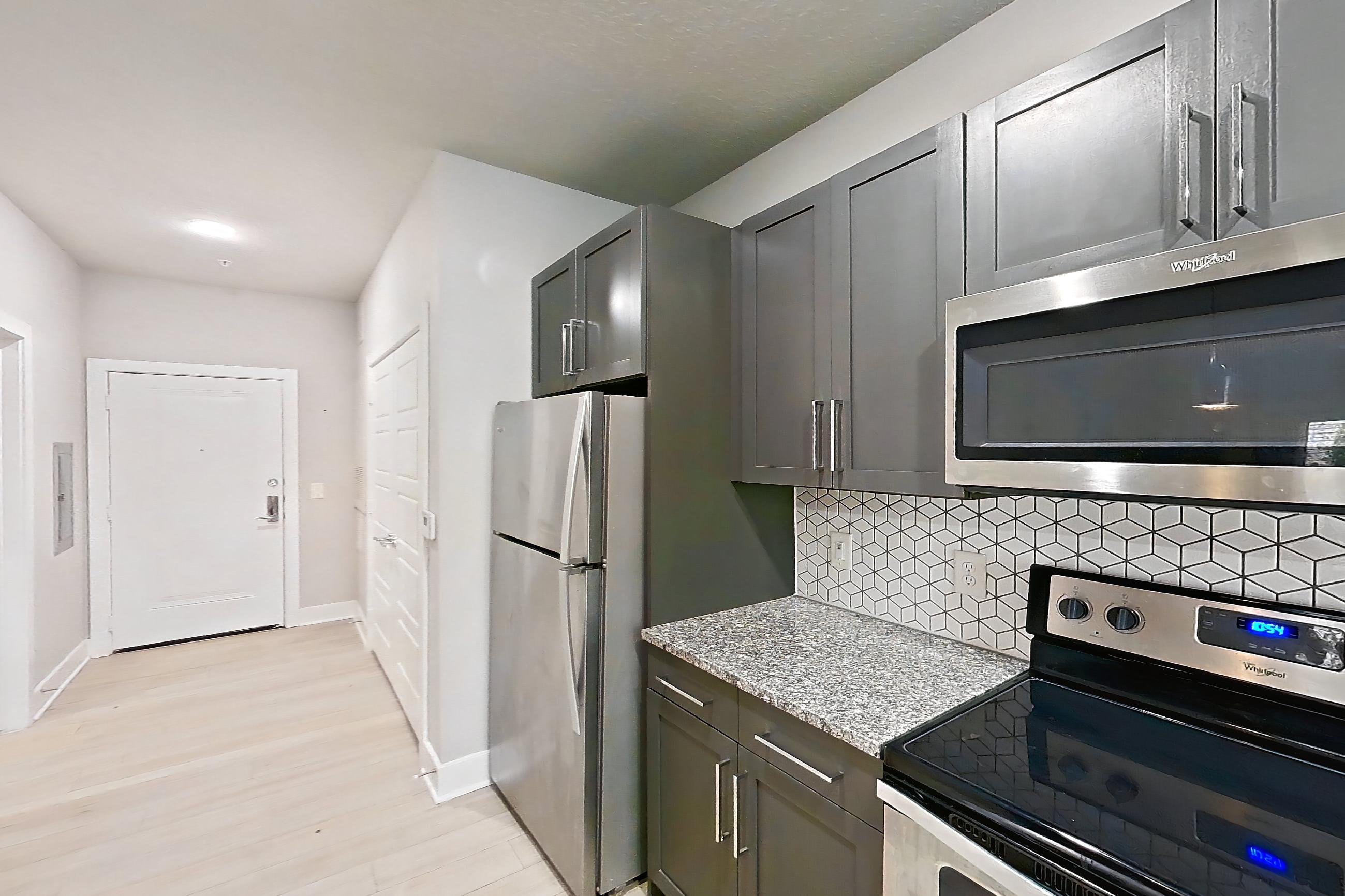 Kitchen with dishwasher, kitchen island, light countertops, light stone countertops, light wood-finish flooring, oven/range, refrigerator, and stainless steel appliances, Apartment 17A-103 at Cortland Reunion