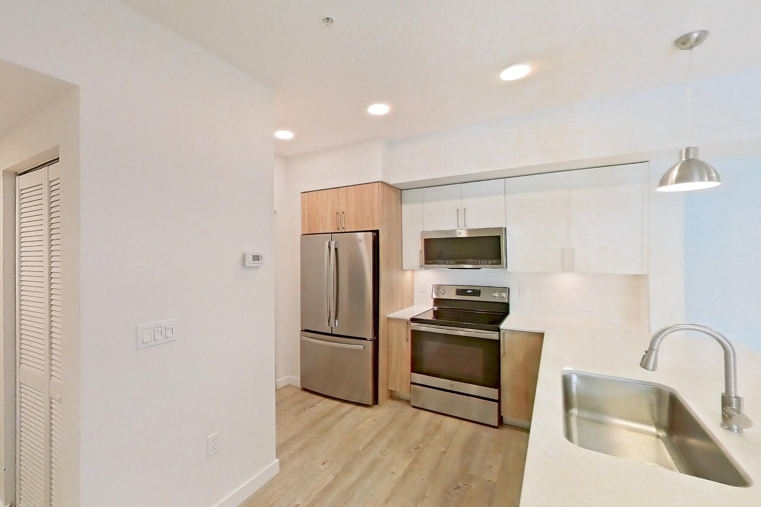 Kitchen entryway with electric range, light countertops, light stone countertops, light wood-finish flooring, oven/range, refrigerator, and stainless steel appliances, Apartment 26-305 at Cortland South Kendall