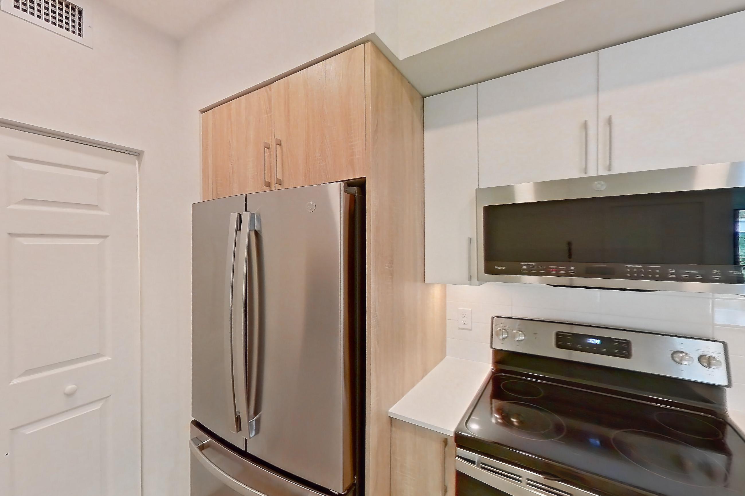 Kitchen with dishwasher, electric range, light countertops, light stone countertops, light wood-finish flooring, microwave, oven/range, refrigerator, and stainless steel appliances, Apartment 26-305 at Cortland South Kendall