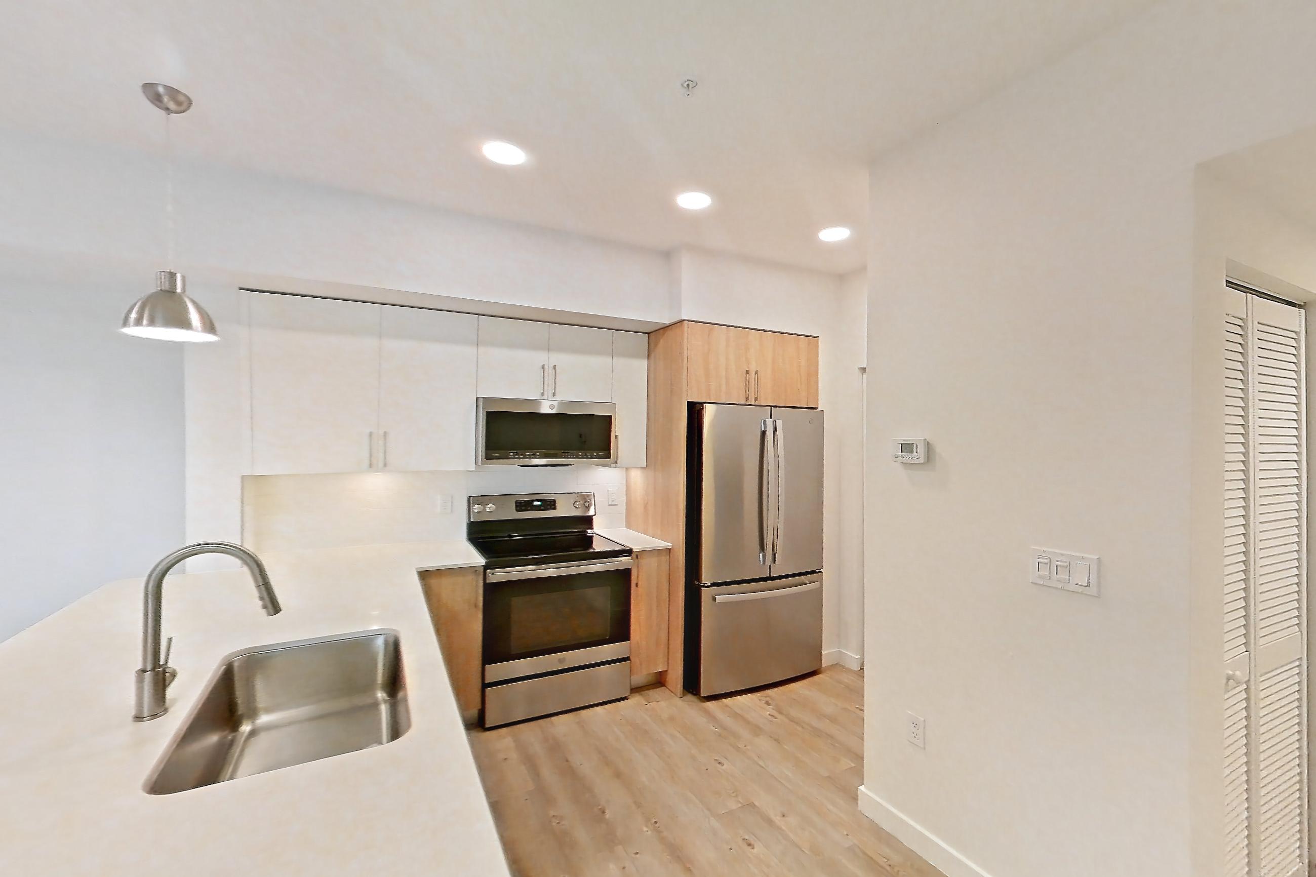 Kitchen entryway with electric range, light countertops, light stone countertops, light wood-finish flooring, oven/range, refrigerator, and stainless steel appliances, Apartment 26-306 at Cortland South Kendall