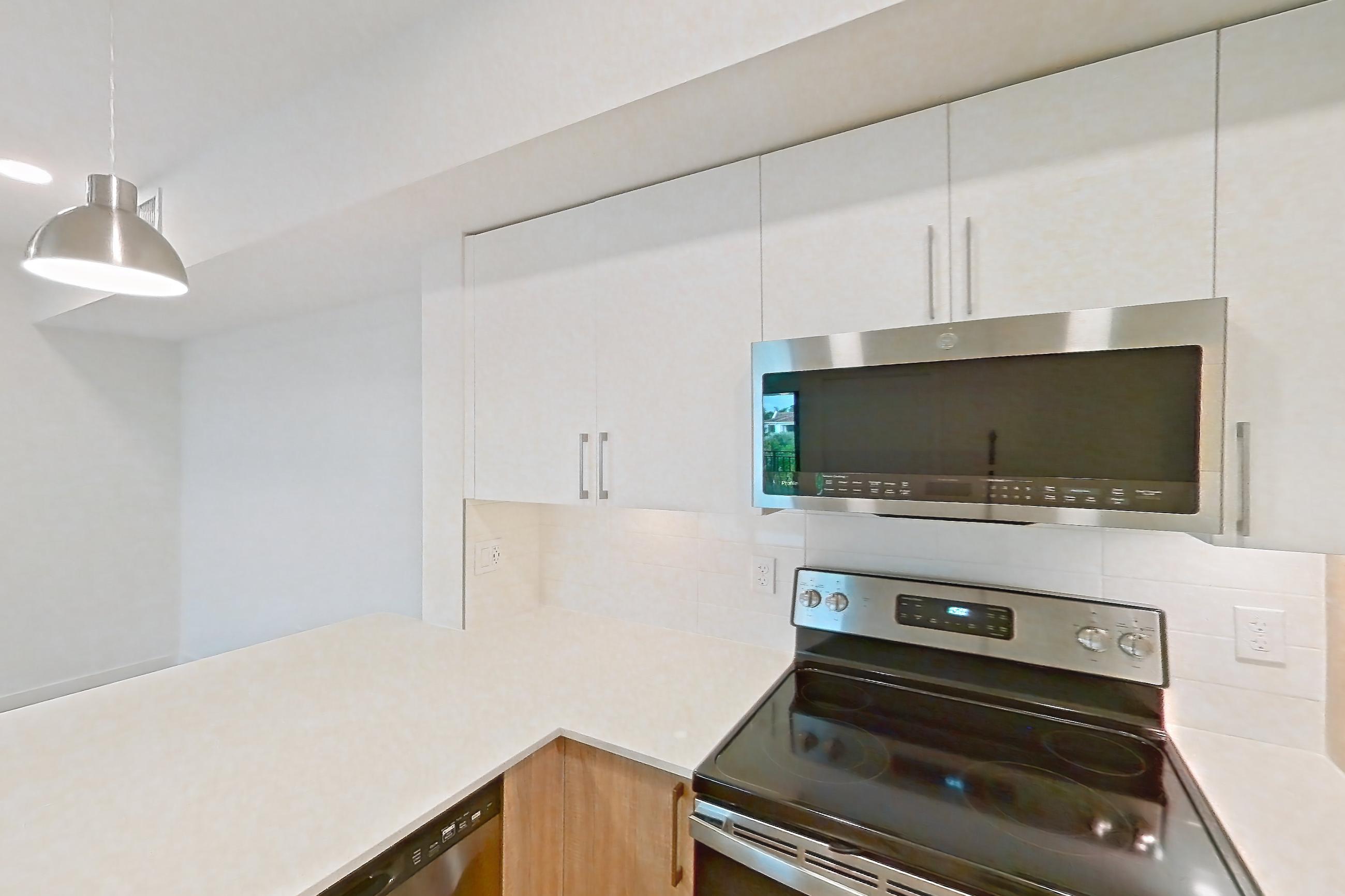 Kitchen with dishwasher, electric range, light countertops, light stone countertops, light wood-finish flooring, microwave, oven/range, refrigerator, and stainless steel appliances, Apartment 26-306 at Cortland South Kendall