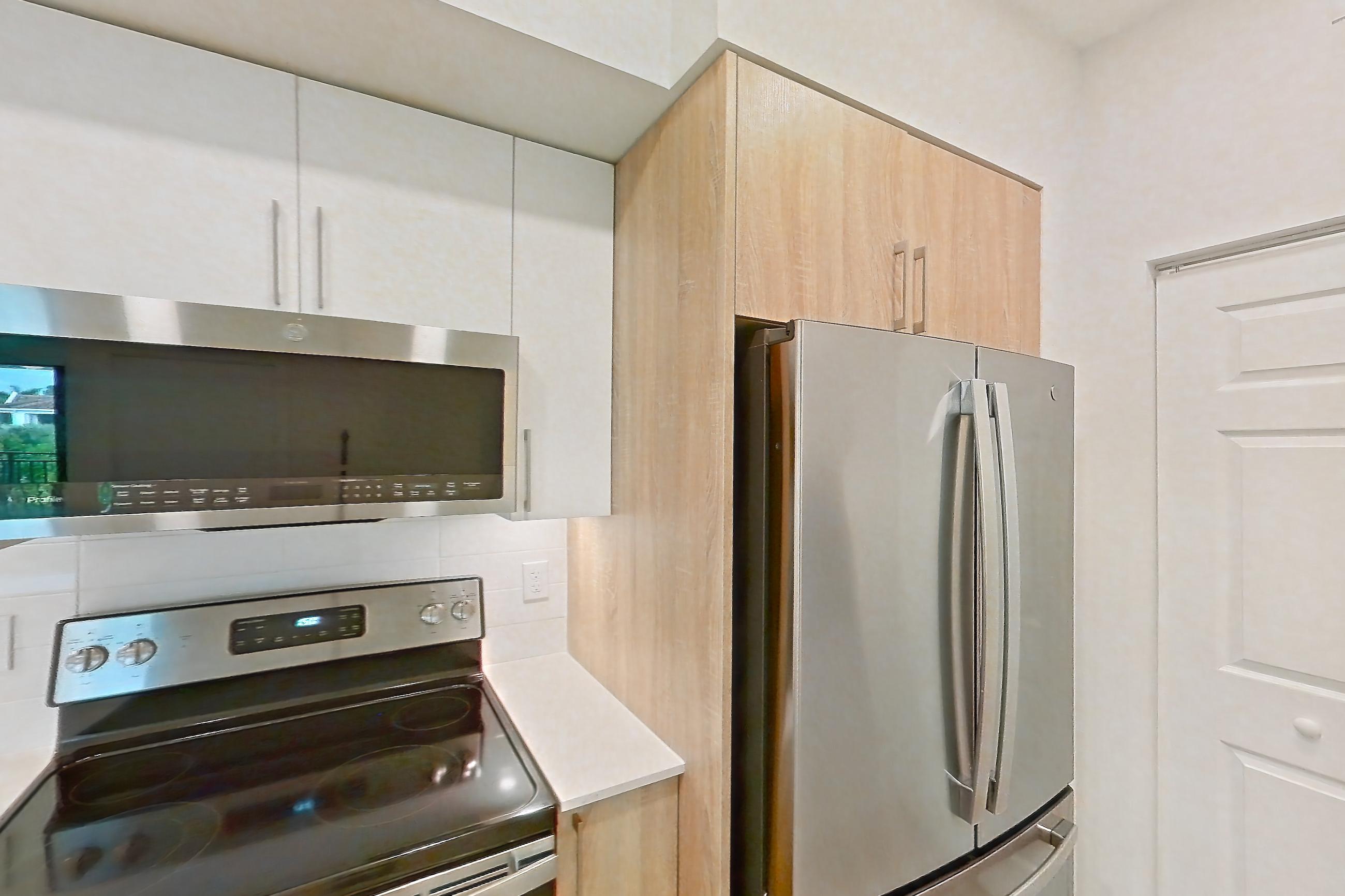 Kitchen with dishwasher, electric range, light countertops, light stone countertops, light wood-finish flooring, microwave, oven/range, refrigerator, and stainless steel appliances, Apartment 26-306 at Cortland South Kendall