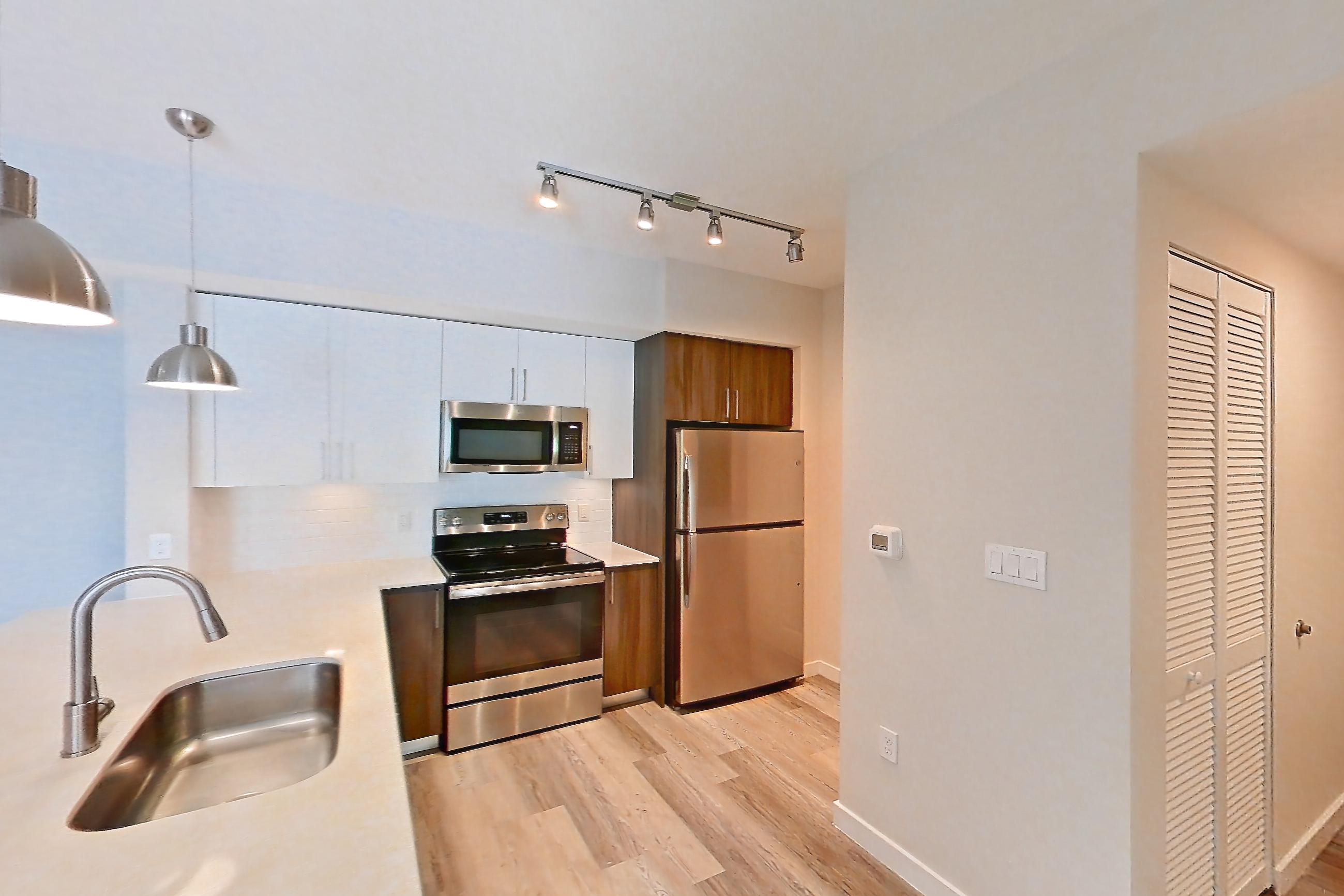Kitchen entryway with electric range, light countertops, light stone countertops, light wood-finish flooring, oven/range, refrigerator, and stainless steel appliances, Apartment 02-303 at Cortland South Kendall