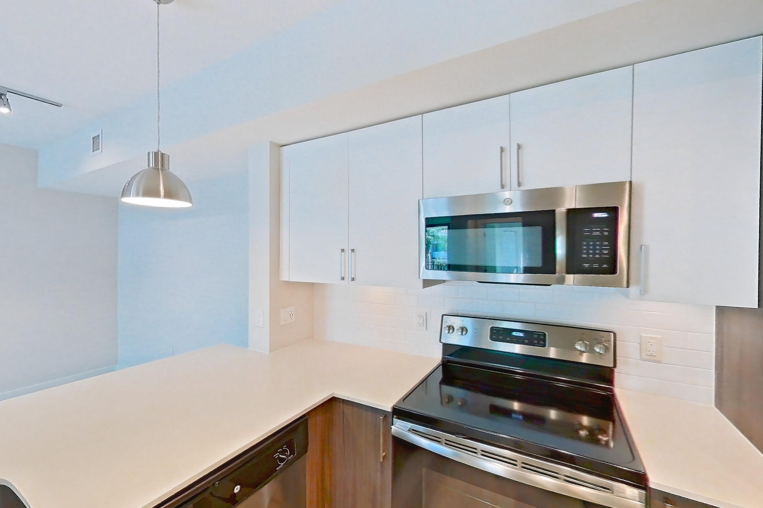 Kitchen with dishwasher, electric range, light countertops, light stone countertops, light wood-finish flooring, microwave, oven/range, range hood, refrigerator, and stainless steel appliances, Apartment 02-303 at Cortland South Kendall