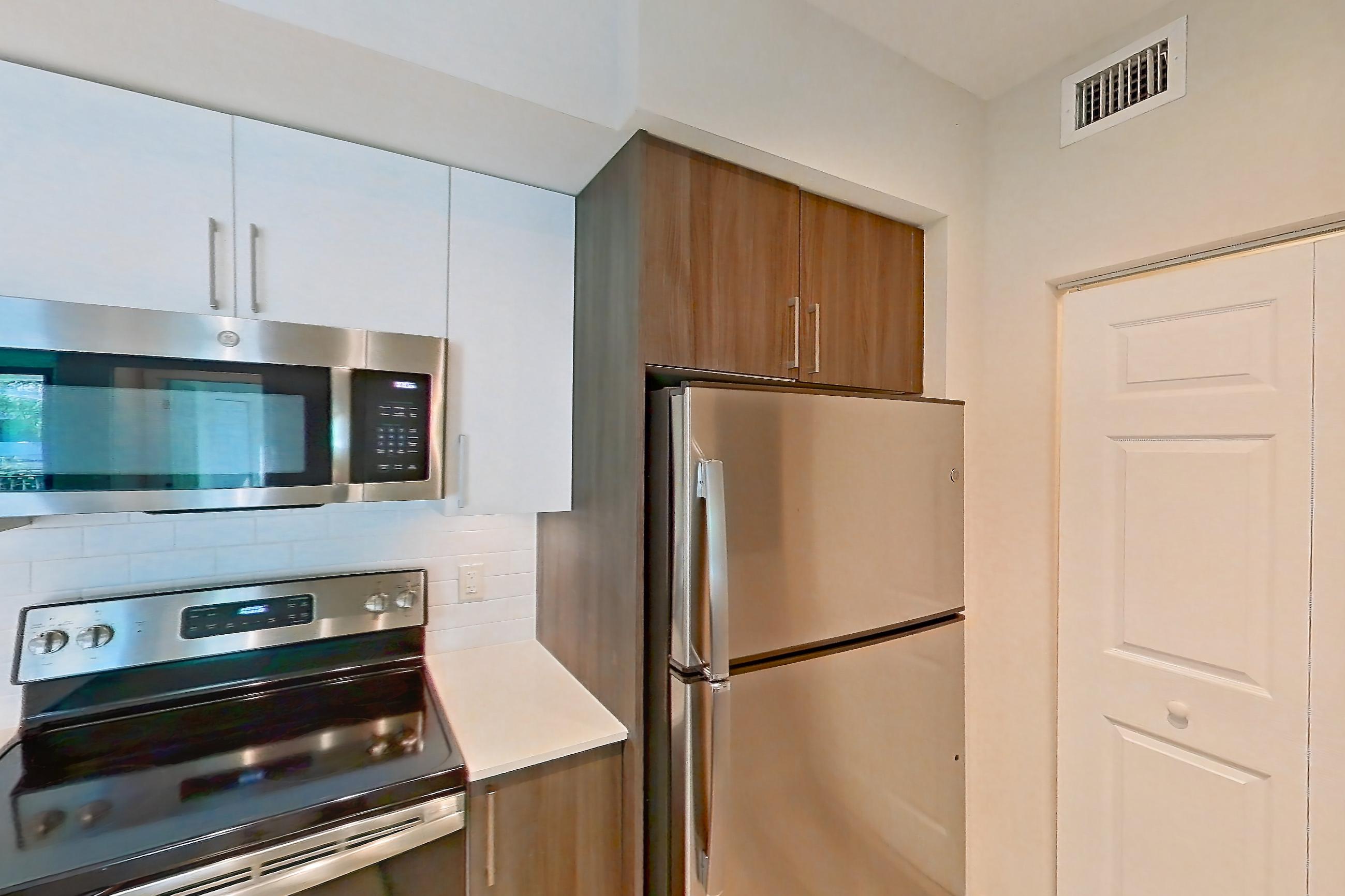 Kitchen with dishwasher, electric range, light countertops, light stone countertops, light wood-finish flooring, microwave, oven/range, range hood, refrigerator, and stainless steel appliances, Apartment 02-303 at Cortland South Kendall