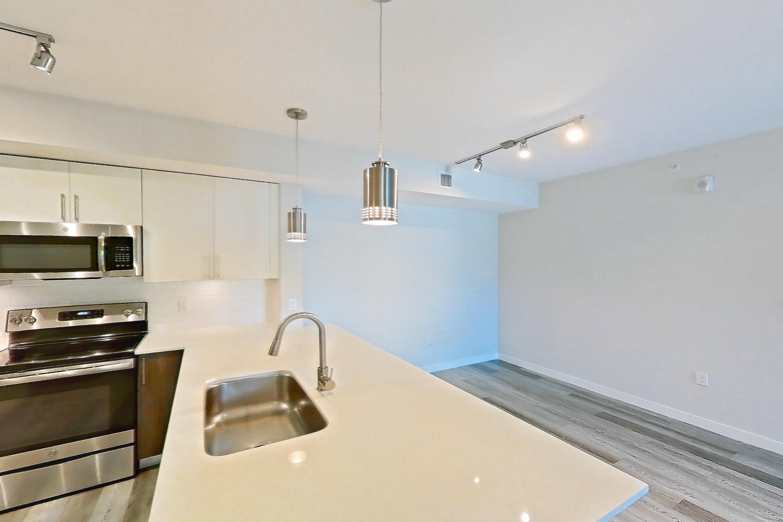 Kitchen entryway with electric range, light countertops, light stone countertops, light wood-finish flooring, oven/range, refrigerator, and stainless steel appliances, Apartment 05-204 at Cortland South Kendall