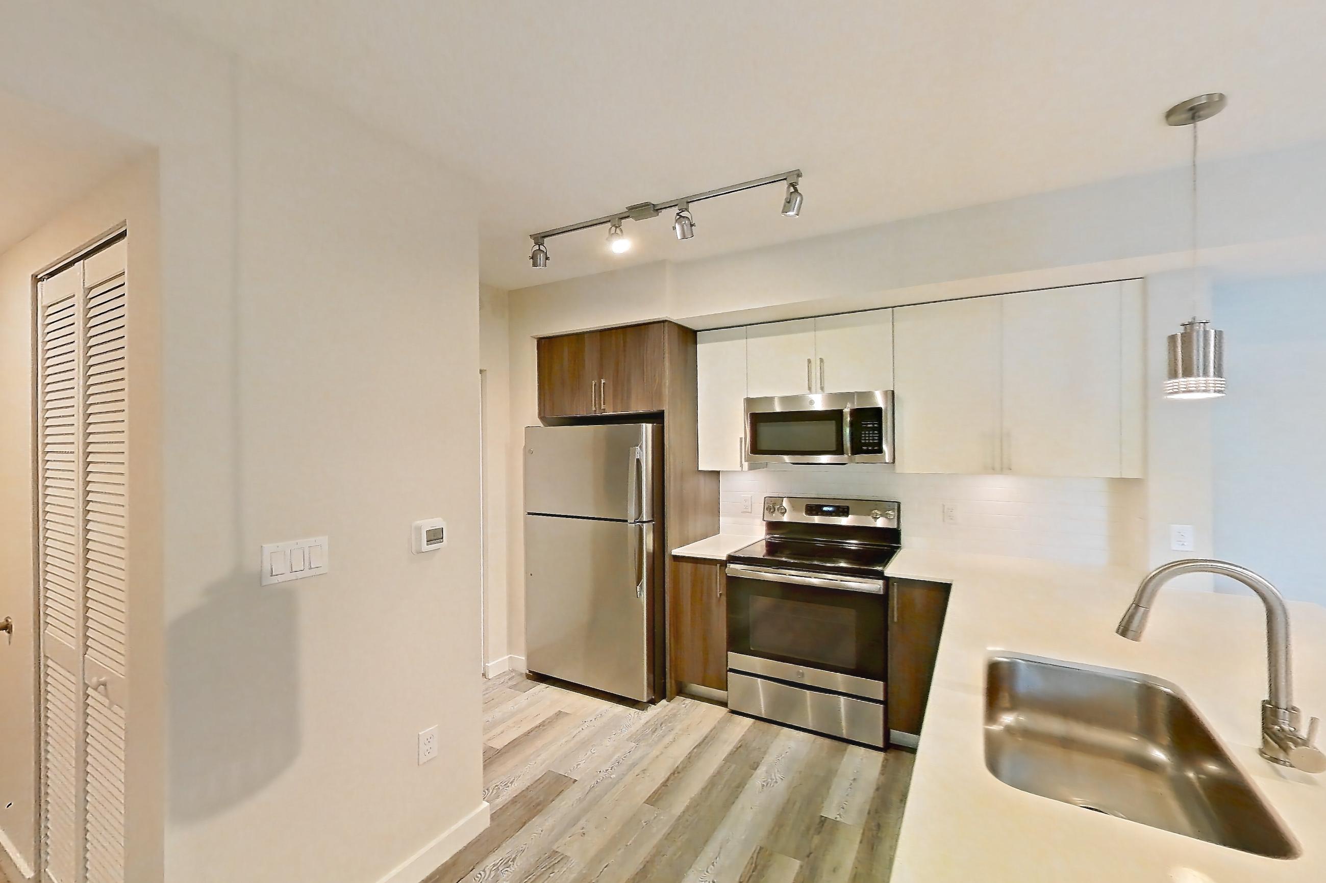 Kitchen entryway with electric range, light countertops, light stone countertops, light wood-finish flooring, oven/range, refrigerator, and stainless steel appliances, Apartment 05-204 at Cortland South Kendall