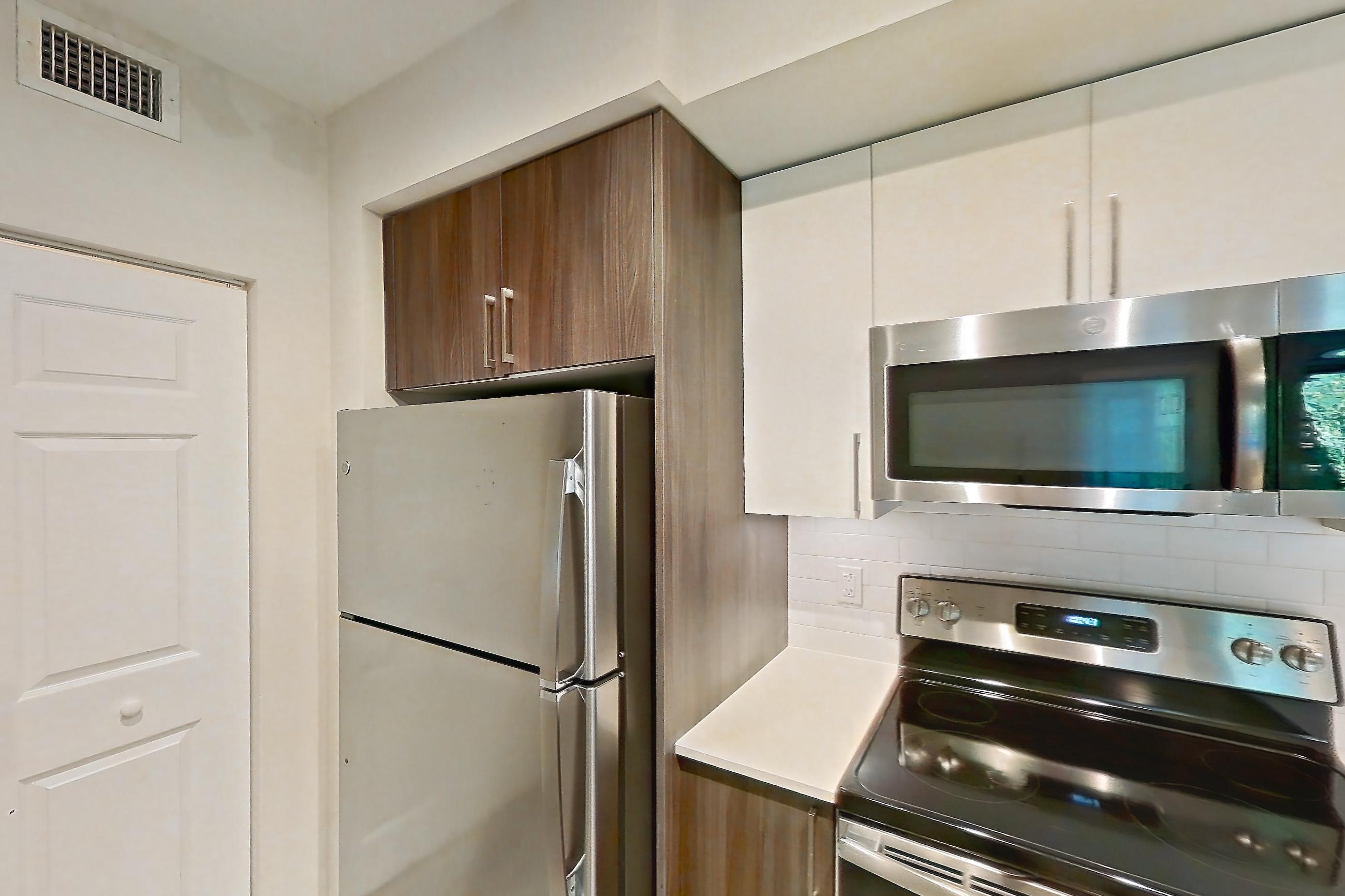 Kitchen with dishwasher, electric range, light countertops, light stone countertops, light wood-finish flooring, microwave, oven/range, refrigerator, and stainless steel appliances, Apartment 05-204 at Cortland South Kendall