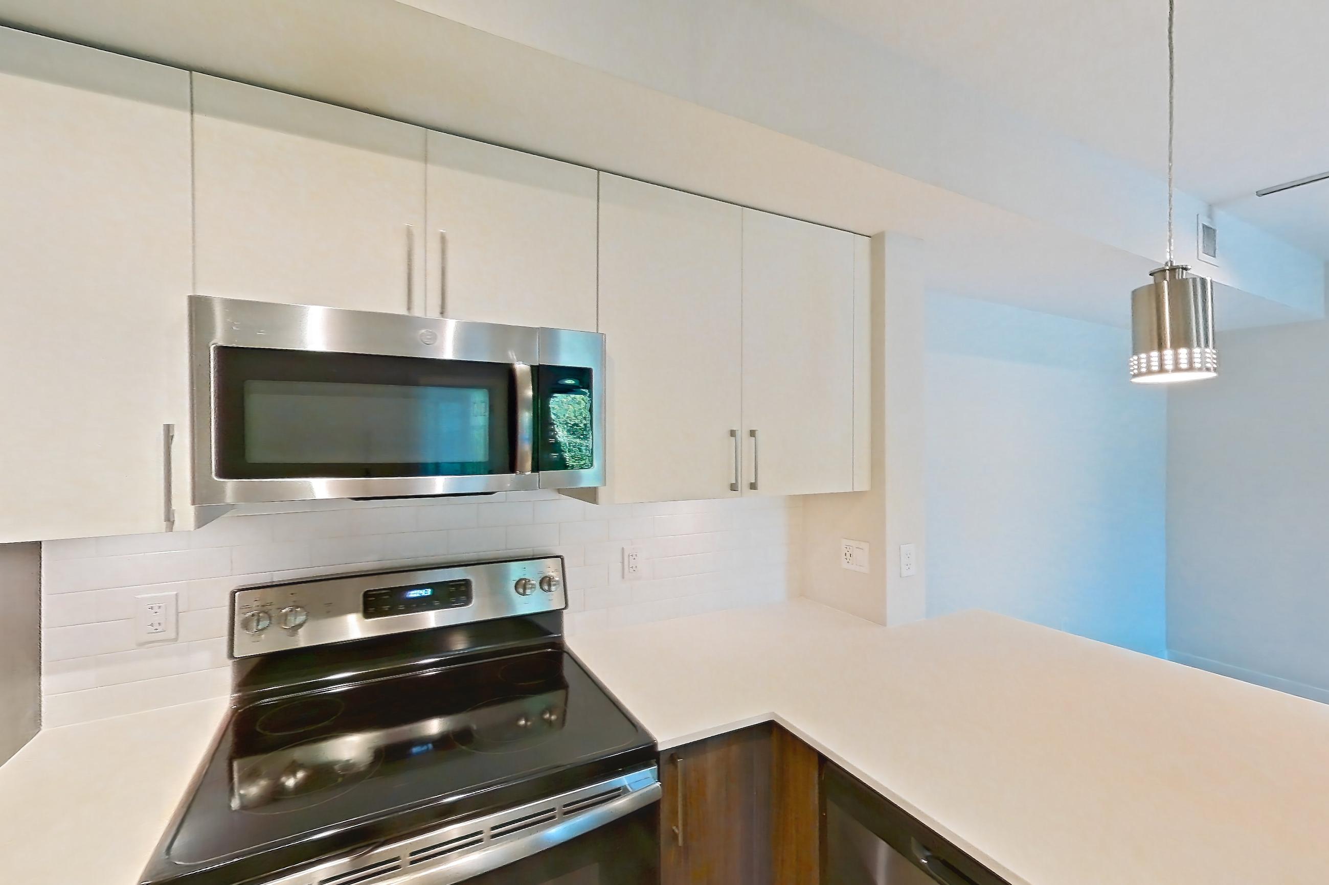 Kitchen with dishwasher, electric range, light countertops, light stone countertops, light wood-finish flooring, microwave, oven/range, refrigerator, and stainless steel appliances, Apartment 05-204 at Cortland South Kendall