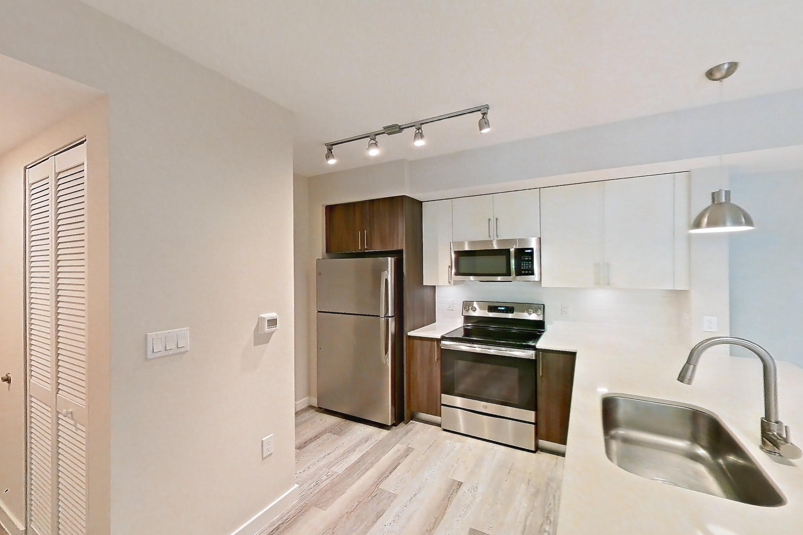 Kitchen entryway with electric range, light countertops, light stone countertops, light wood-finish flooring, oven/range, refrigerator, and stainless steel appliances, Apartment 05-205 at Cortland South Kendall