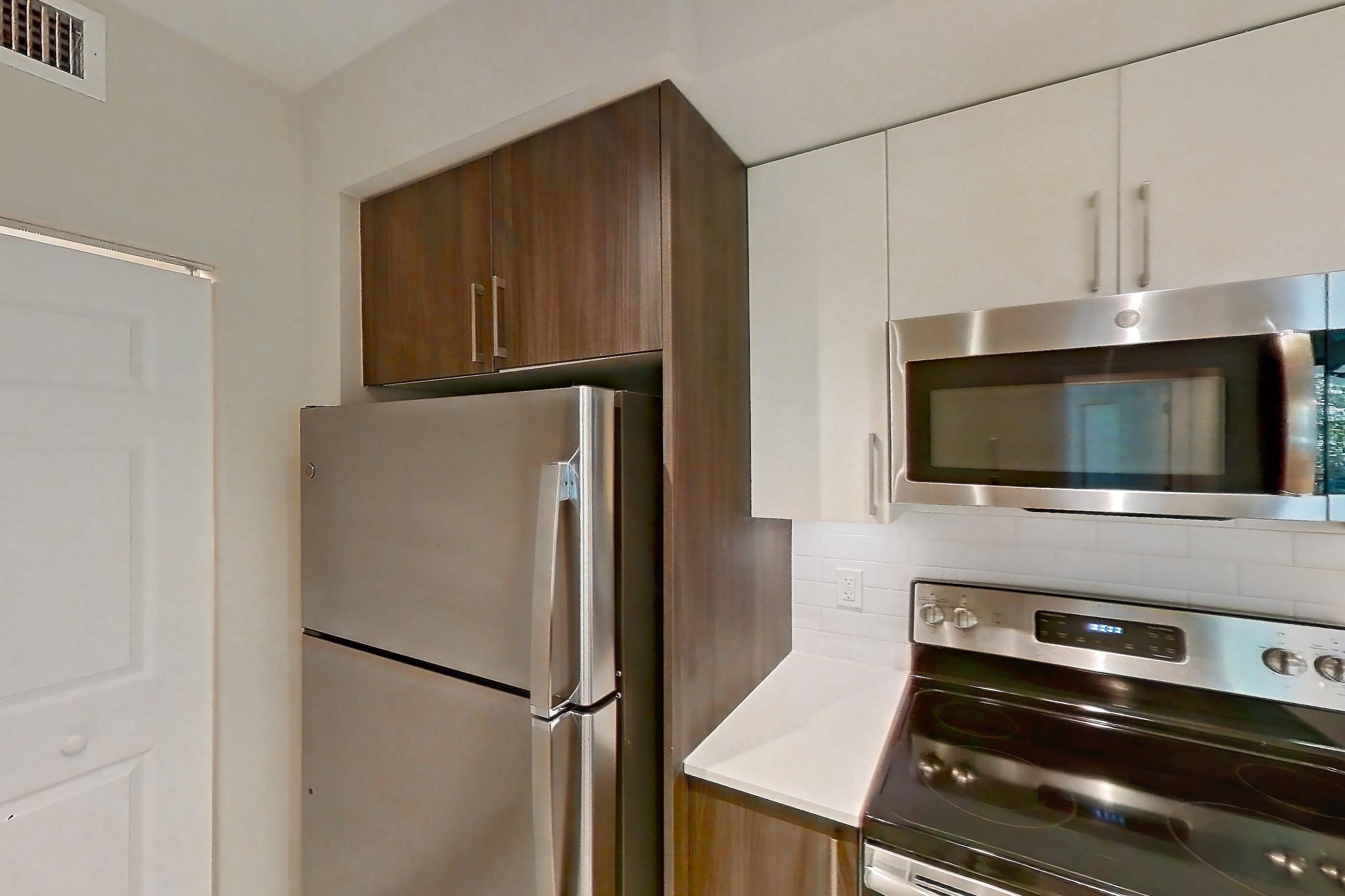 Kitchen with dishwasher, electric range, light countertops, light stone countertops, light wood-finish flooring, microwave, oven/range, refrigerator, and stainless steel appliances, Apartment 05-205 at Cortland South Kendall