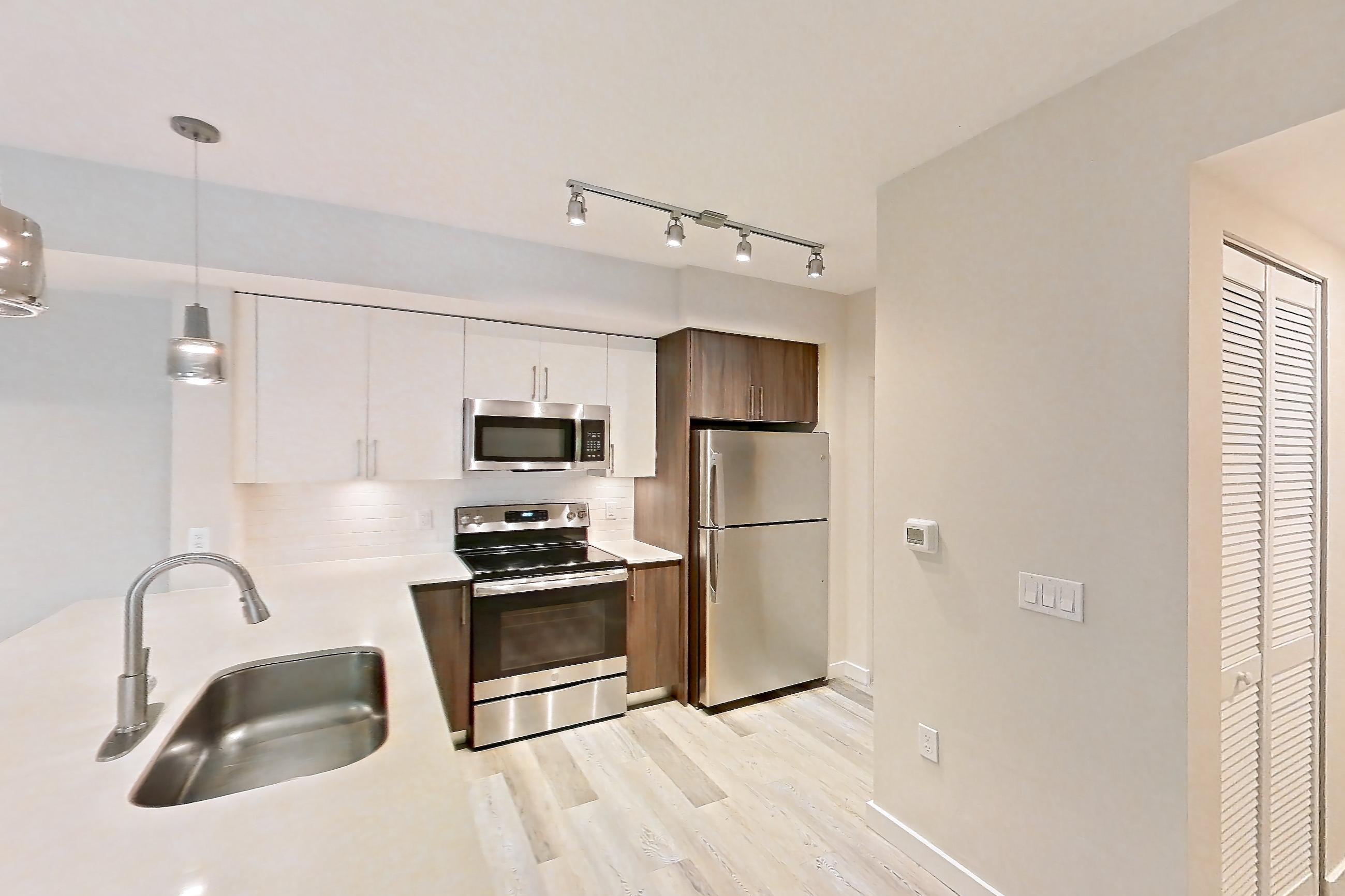 Kitchen entryway with electric range, light countertops, light stone countertops, light wood-finish flooring, oven/range, refrigerator, and stainless steel appliances, Apartment 06-102 at Cortland South Kendall