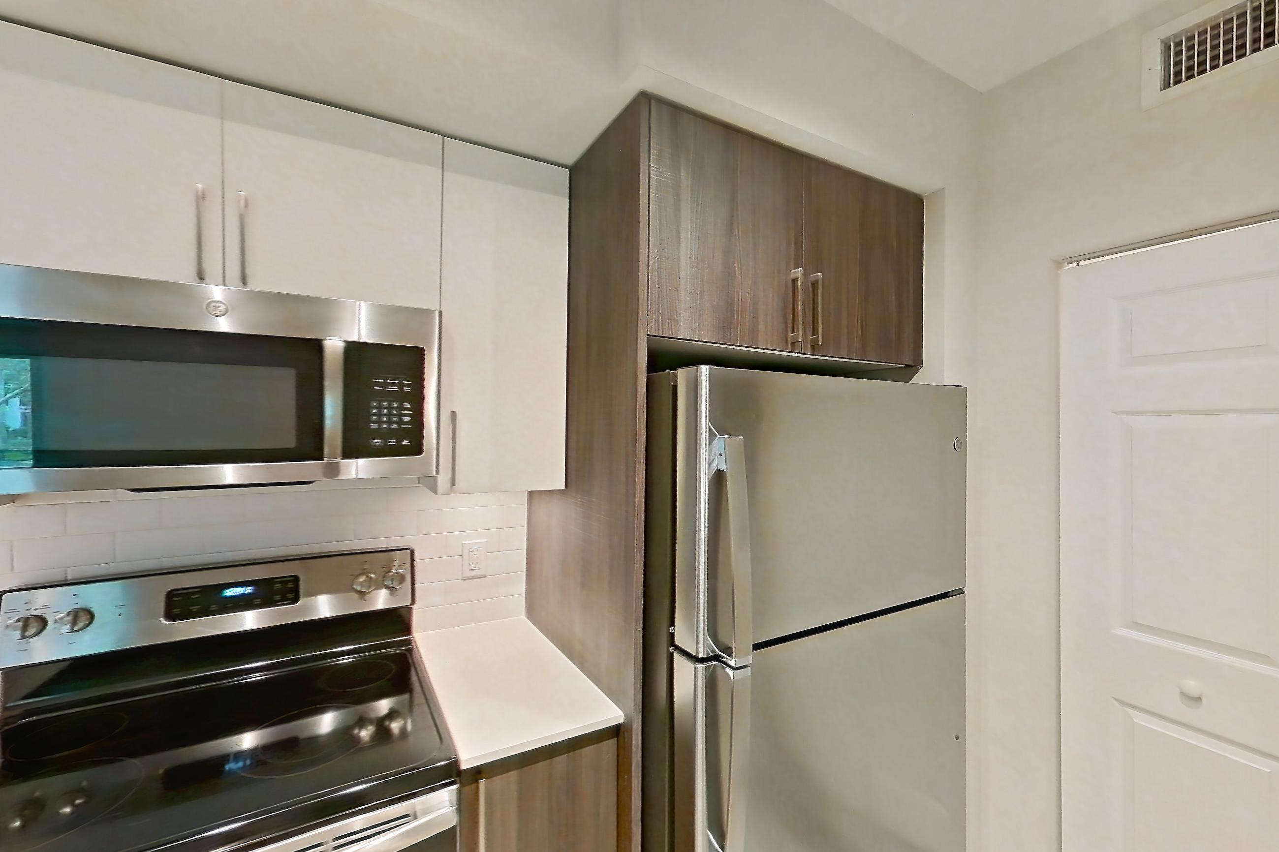 Kitchen with dishwasher, electric range, light countertops, light stone countertops, light wood-finish flooring, microwave, oven/range, range hood, refrigerator, and stainless steel appliances, Apartment 06-102 at Cortland South Kendall