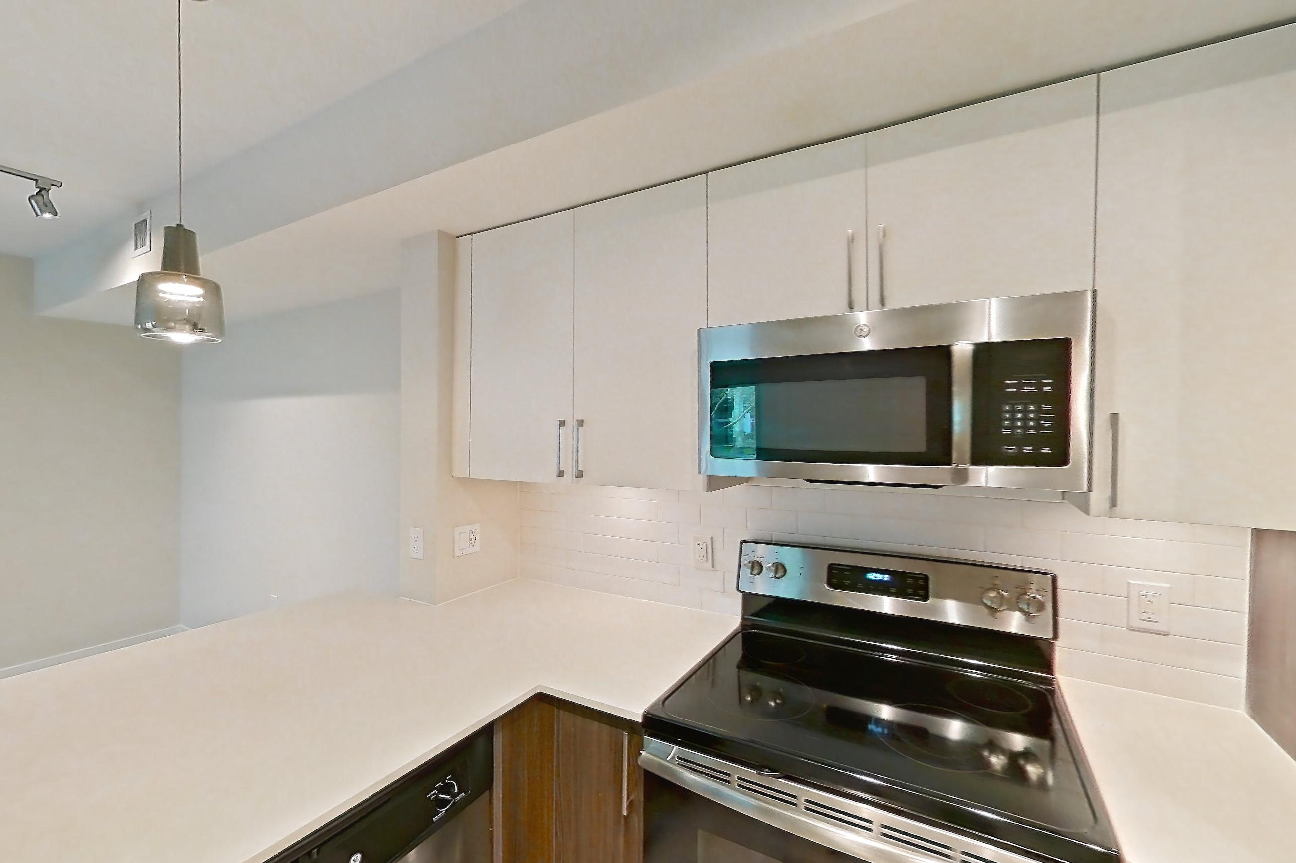 Kitchen with dishwasher, electric range, light countertops, light stone countertops, light wood-finish flooring, microwave, oven/range, range hood, refrigerator, and stainless steel appliances, Apartment 06-102 at Cortland South Kendall