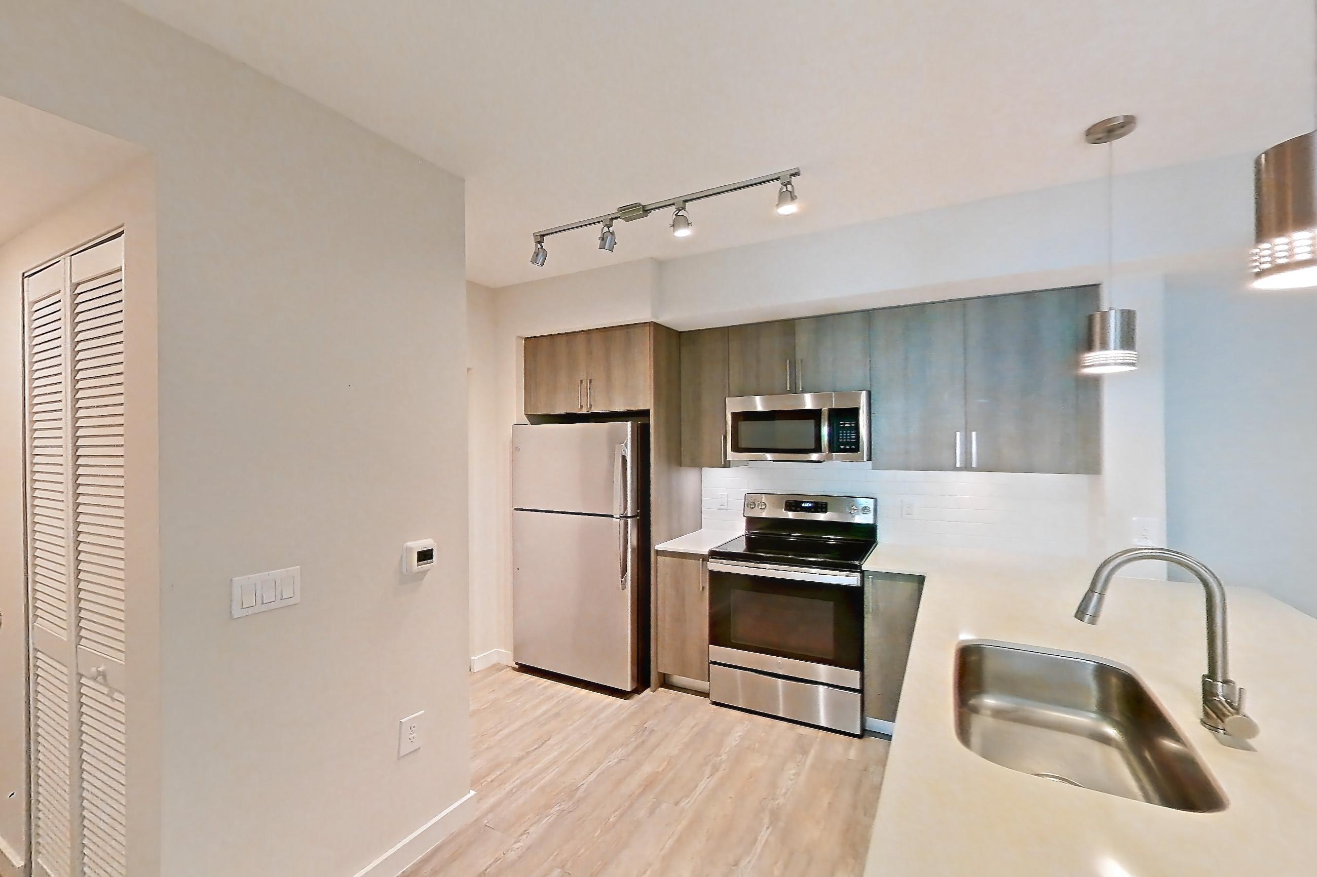 Kitchen entryway with electric range, light countertops, light stone countertops, light wood-finish flooring, oven/range, refrigerator, and stainless steel appliances, Apartment 10-101 at Cortland South Kendall