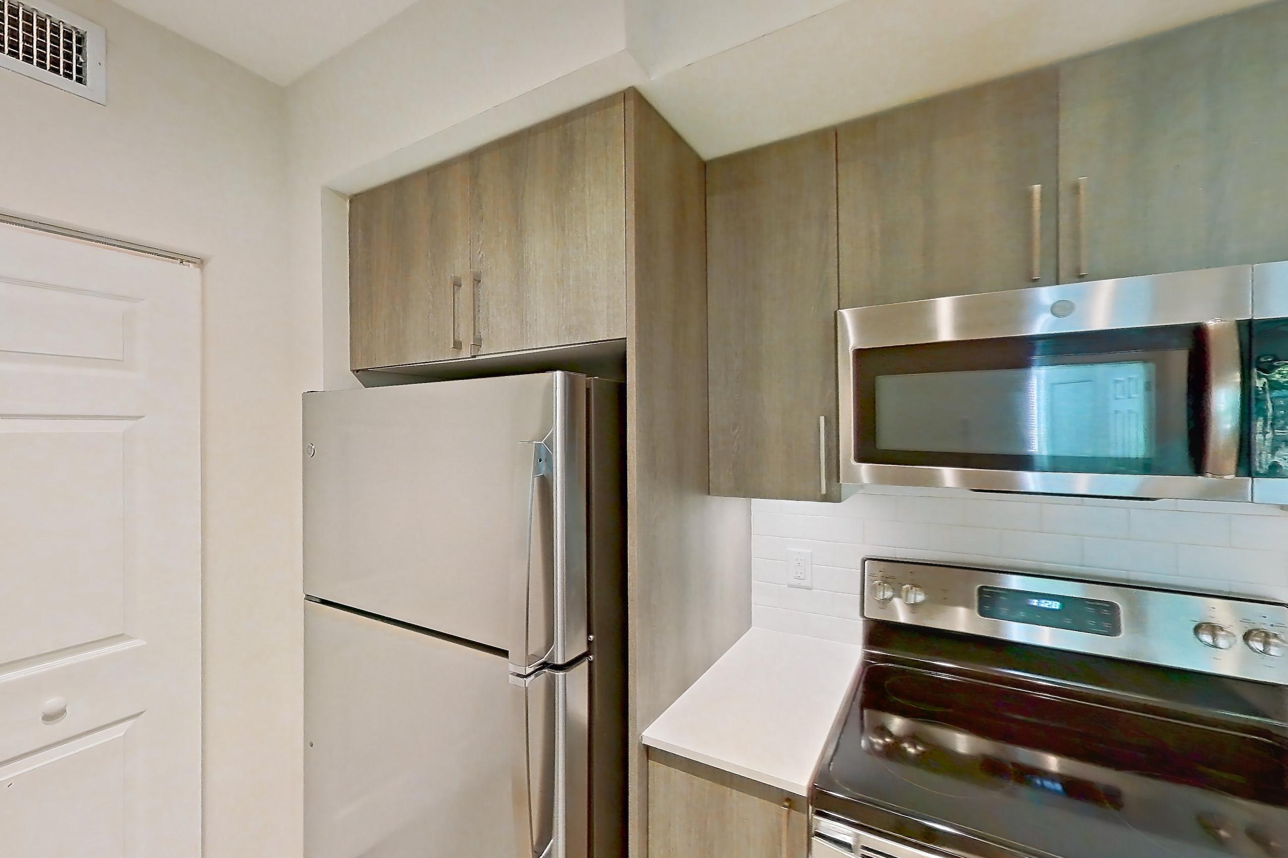 Kitchen with dishwasher, electric range, light countertops, light stone countertops, light wood-finish flooring, microwave, oven/range, refrigerator, and stainless steel appliances, Apartment 10-101 at Cortland South Kendall