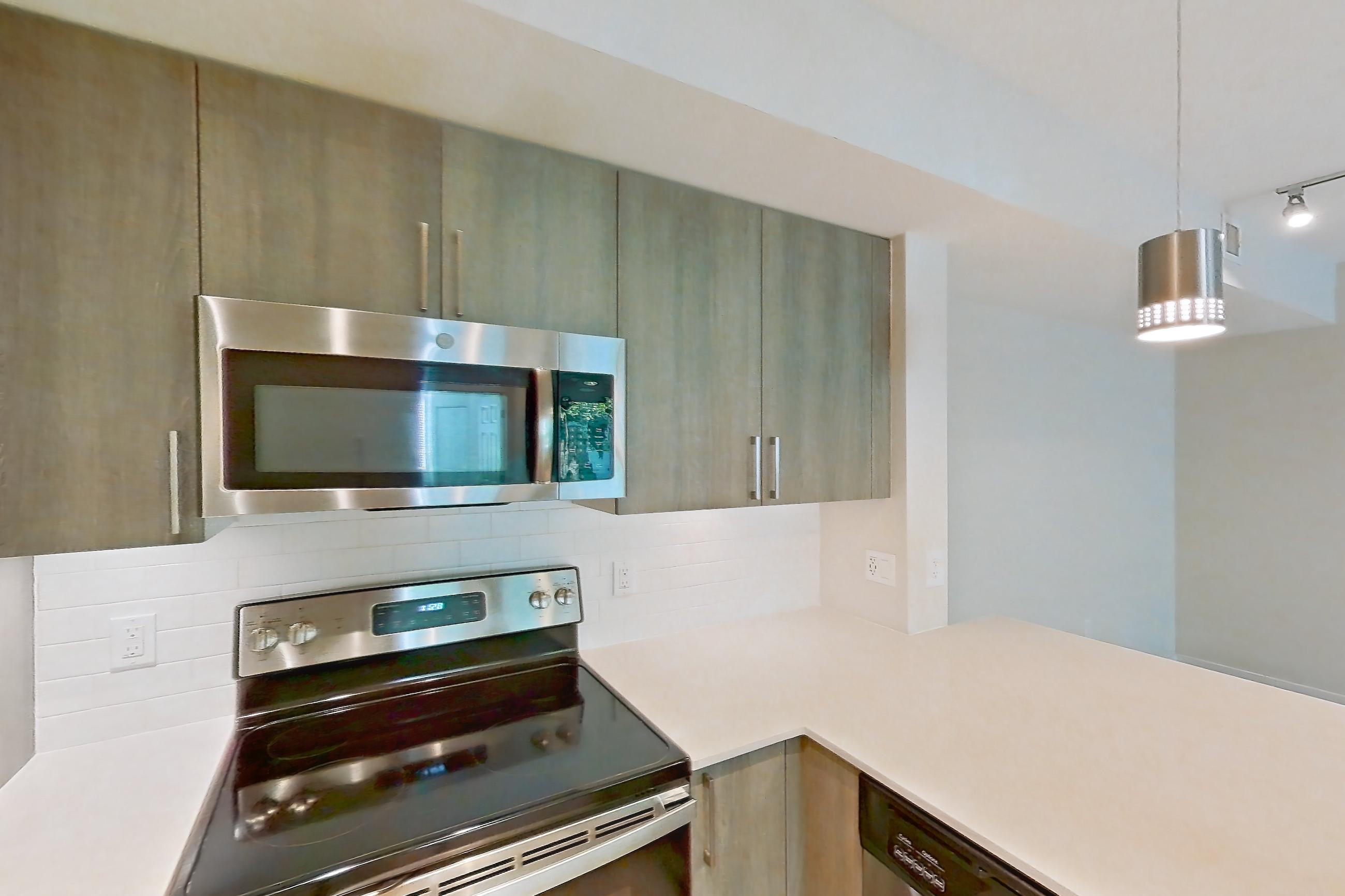 Kitchen with dishwasher, electric range, light countertops, light stone countertops, light wood-finish flooring, microwave, oven/range, refrigerator, and stainless steel appliances, Apartment 10-101 at Cortland South Kendall