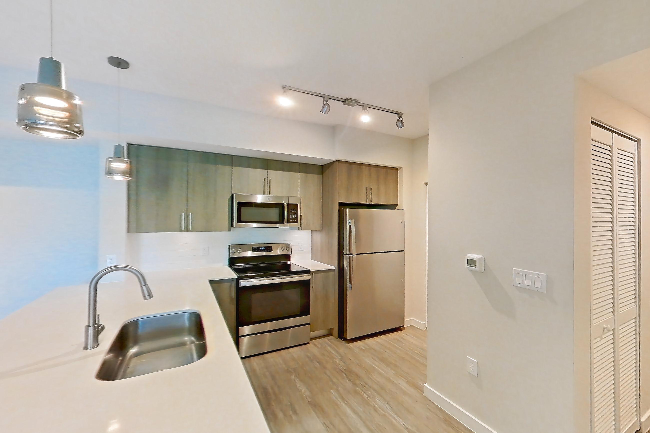 Kitchen entryway with electric range, light stone countertops, light wood-finish flooring, oven/range, refrigerator, and stainless steel appliances, Apartment 11-307 at Cortland South Kendall