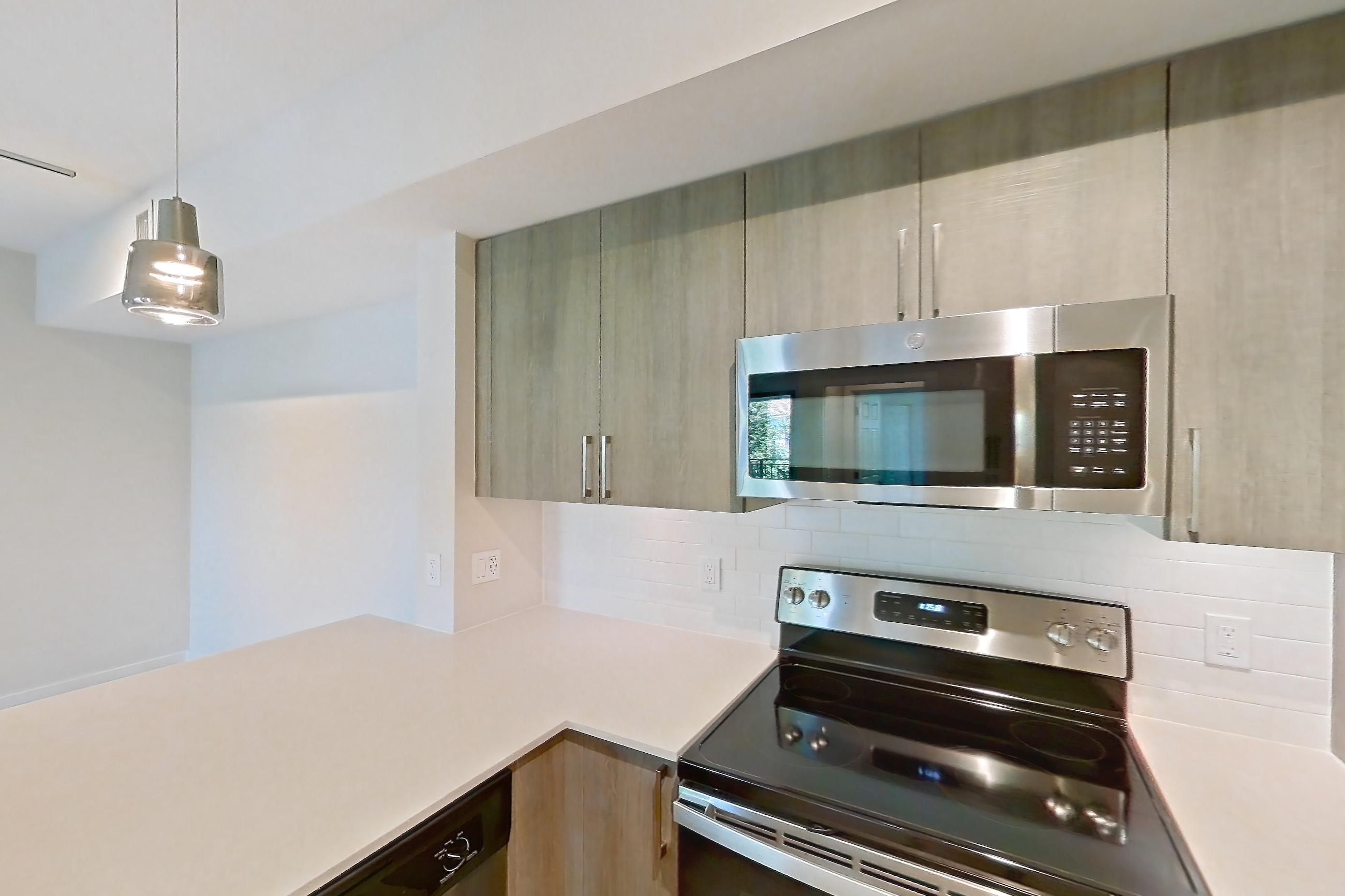Kitchen with dishwasher, electric range, light countertops, light stone countertops, light wood-finish flooring, microwave, oven/range, refrigerator, and stainless steel appliances, Apartment 11-307 at Cortland South Kendall