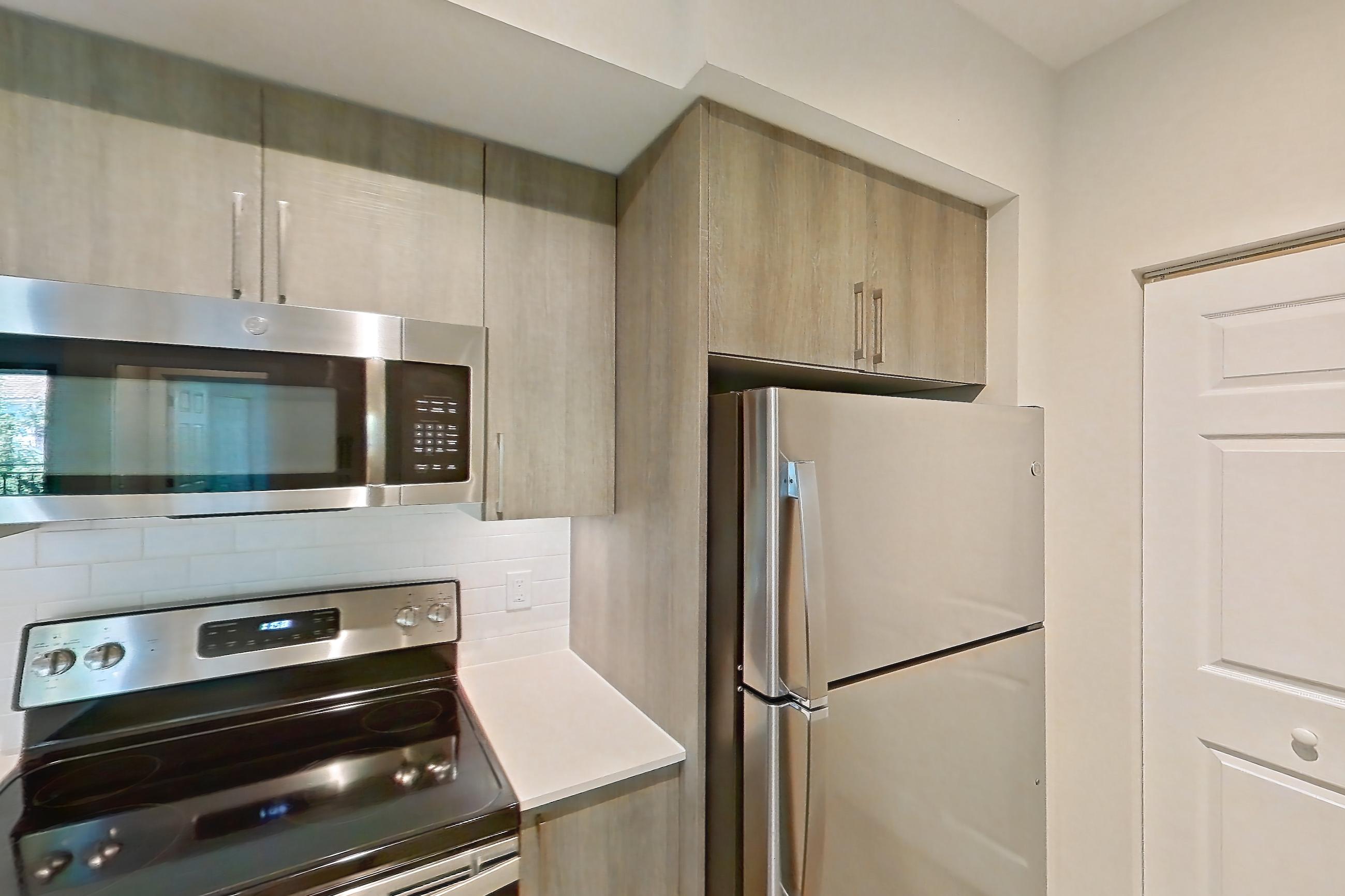 Kitchen with dishwasher, electric range, light countertops, light stone countertops, light wood-finish flooring, microwave, oven/range, refrigerator, and stainless steel appliances, Apartment 11-307 at Cortland South Kendall