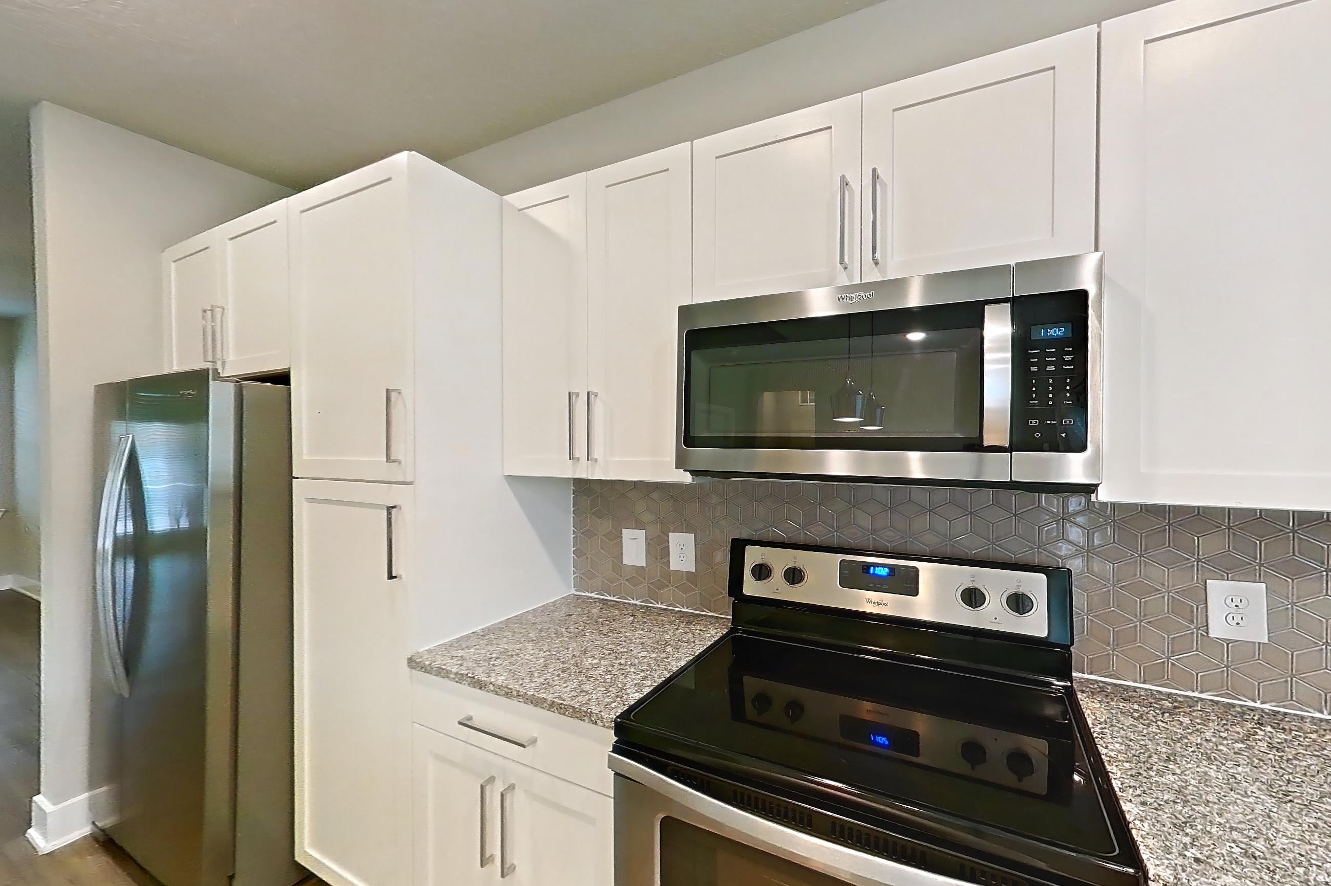 Kitchen with dark wood-finish flooring, dishwasher, electric range, light countertops, light stone countertops, light wood-finish flooring, oven/range, refrigerator, and stainless steel appliances, Apartment 04-186 at Cortland Reunion