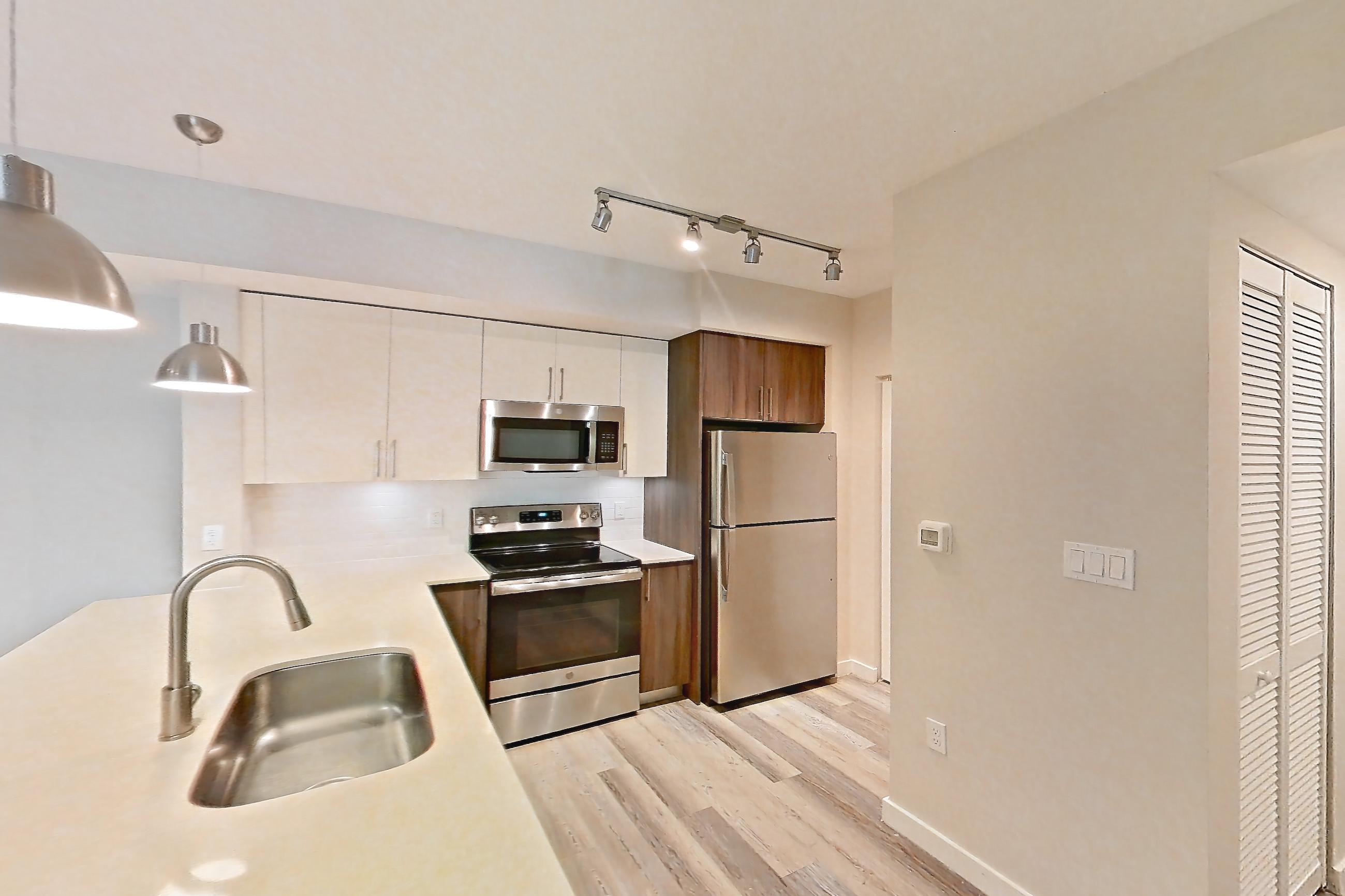 Kitchen entryway with electric range, light countertops, light stone countertops, light wood-finish flooring, oven/range, range hood, refrigerator, and stainless steel appliances, Apartment 13-203 at Cortland South Kendall
