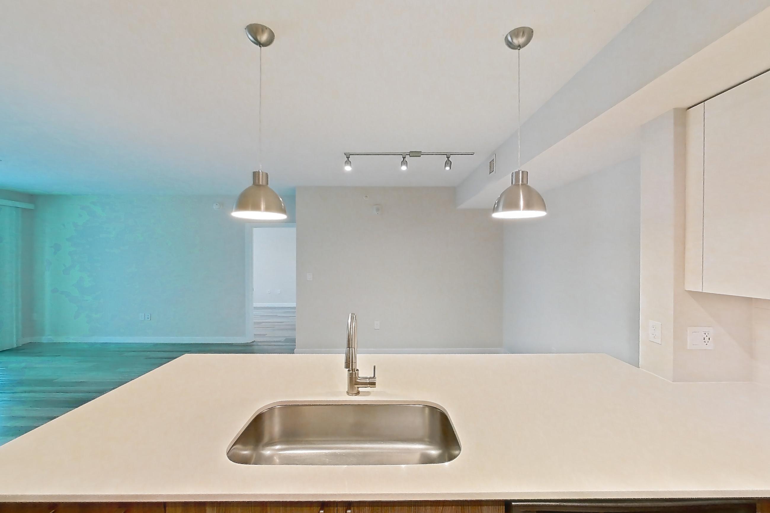 Kitchen with dishwasher, electric range, light countertops, light stone countertops, light wood-finish flooring, microwave, oven/range, range hood, refrigerator, and stainless steel appliances, Apartment 13-203 at Cortland South Kendall