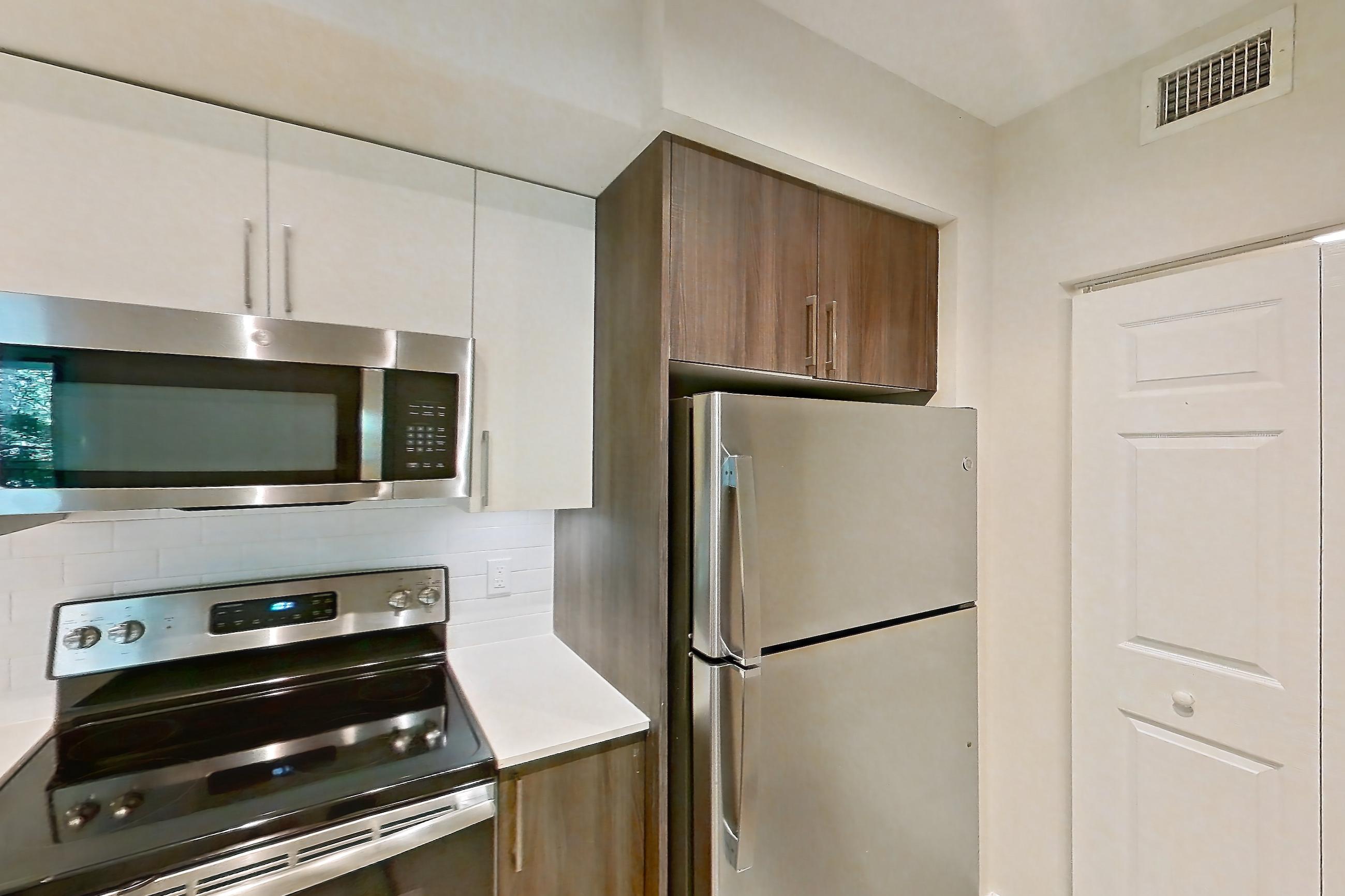 Kitchen with dishwasher, electric range, light countertops, light stone countertops, light wood-finish flooring, microwave, oven/range, range hood, refrigerator, and stainless steel appliances, Apartment 13-203 at Cortland South Kendall