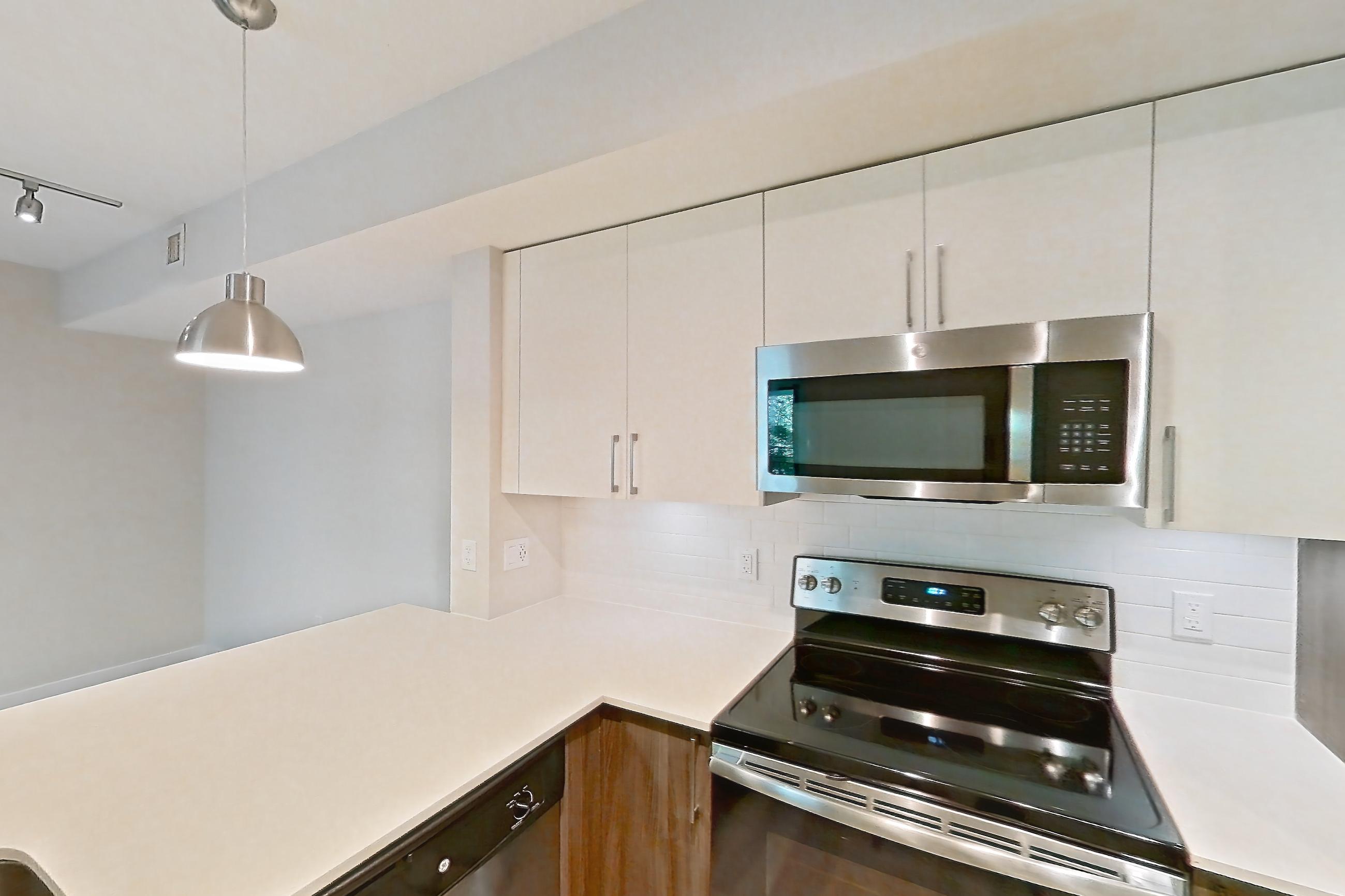 Kitchen with dishwasher, electric range, light countertops, light stone countertops, light wood-finish flooring, microwave, oven/range, range hood, refrigerator, and stainless steel appliances, Apartment 13-203 at Cortland South Kendall
