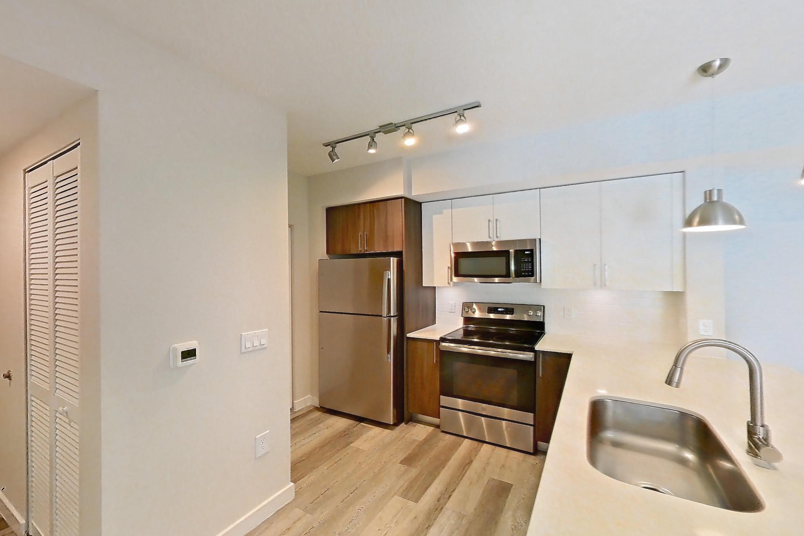 Kitchen entryway with electric range, light countertops, light stone countertops, light wood-finish flooring, oven/range, refrigerator, and stainless steel appliances, Apartment 15-108 at Cortland South Kendall