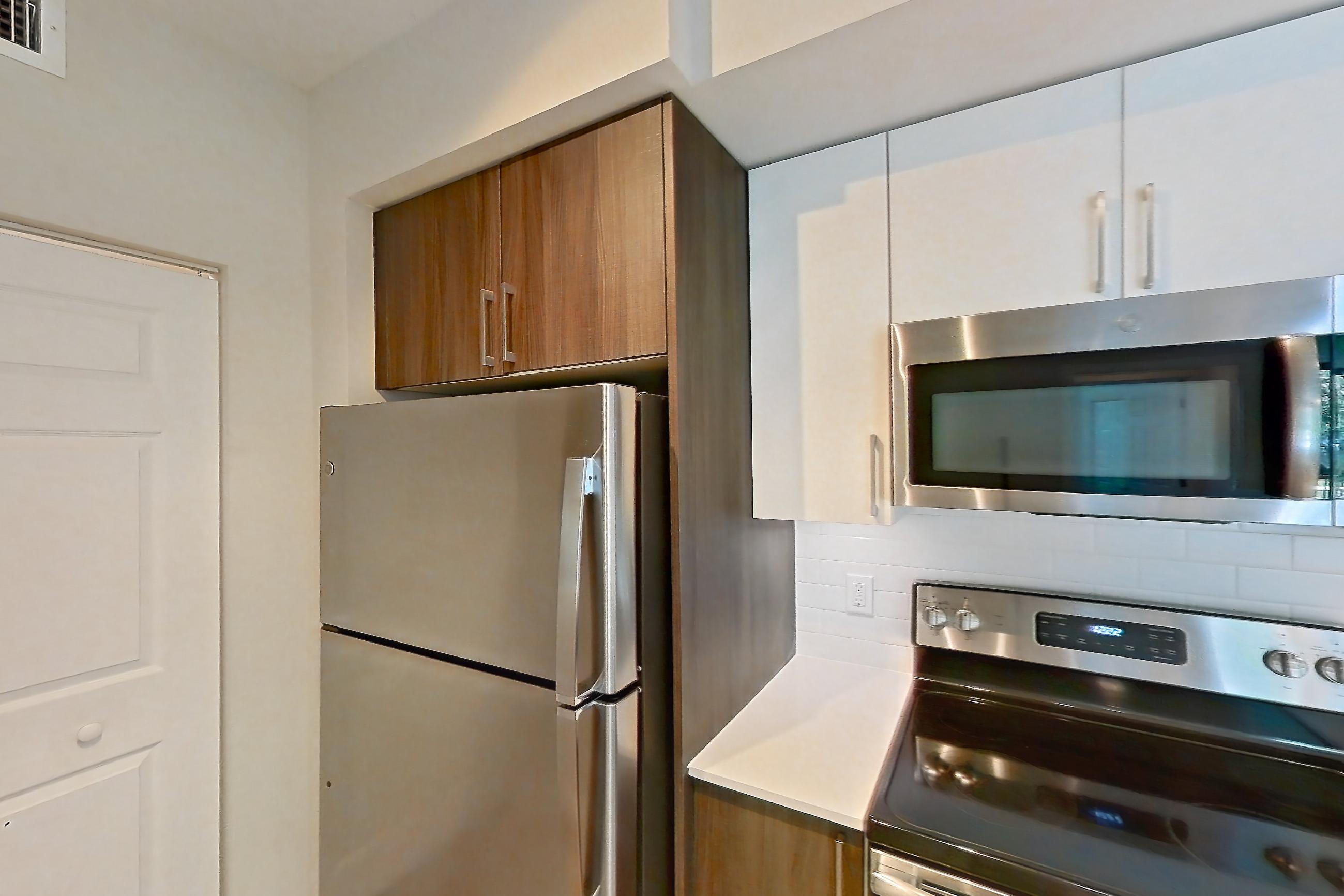 Kitchen with dishwasher, electric range, light countertops, light stone countertops, light wood-finish flooring, microwave, oven/range, refrigerator, and stainless steel appliances, Apartment 15-108 at Cortland South Kendall