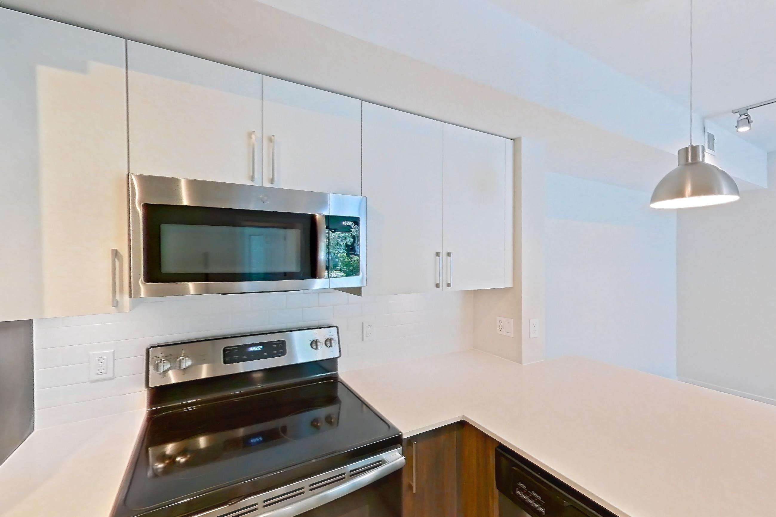 Kitchen with dishwasher, electric range, light countertops, light stone countertops, light wood-finish flooring, microwave, oven/range, refrigerator, and stainless steel appliances, Apartment 15-108 at Cortland South Kendall