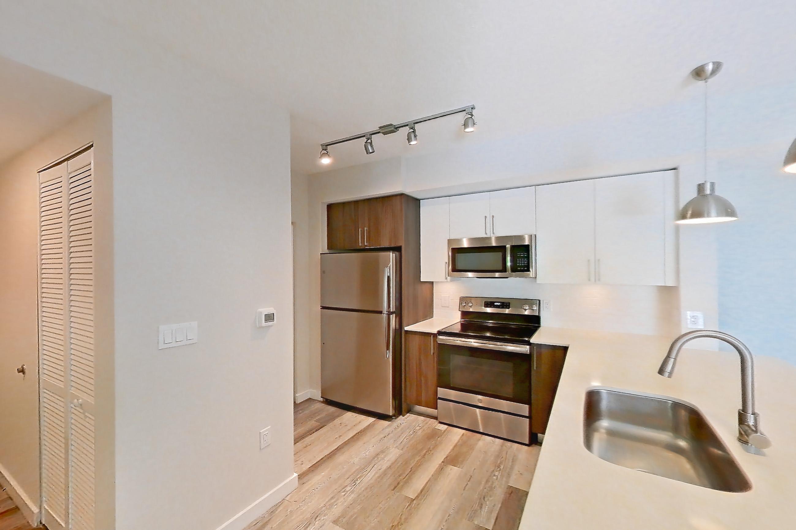Kitchen entryway with electric range, light countertops, light stone countertops, light wood-finish flooring, oven/range, refrigerator, and stainless steel appliances, Apartment 17-205 at Cortland South Kendall
