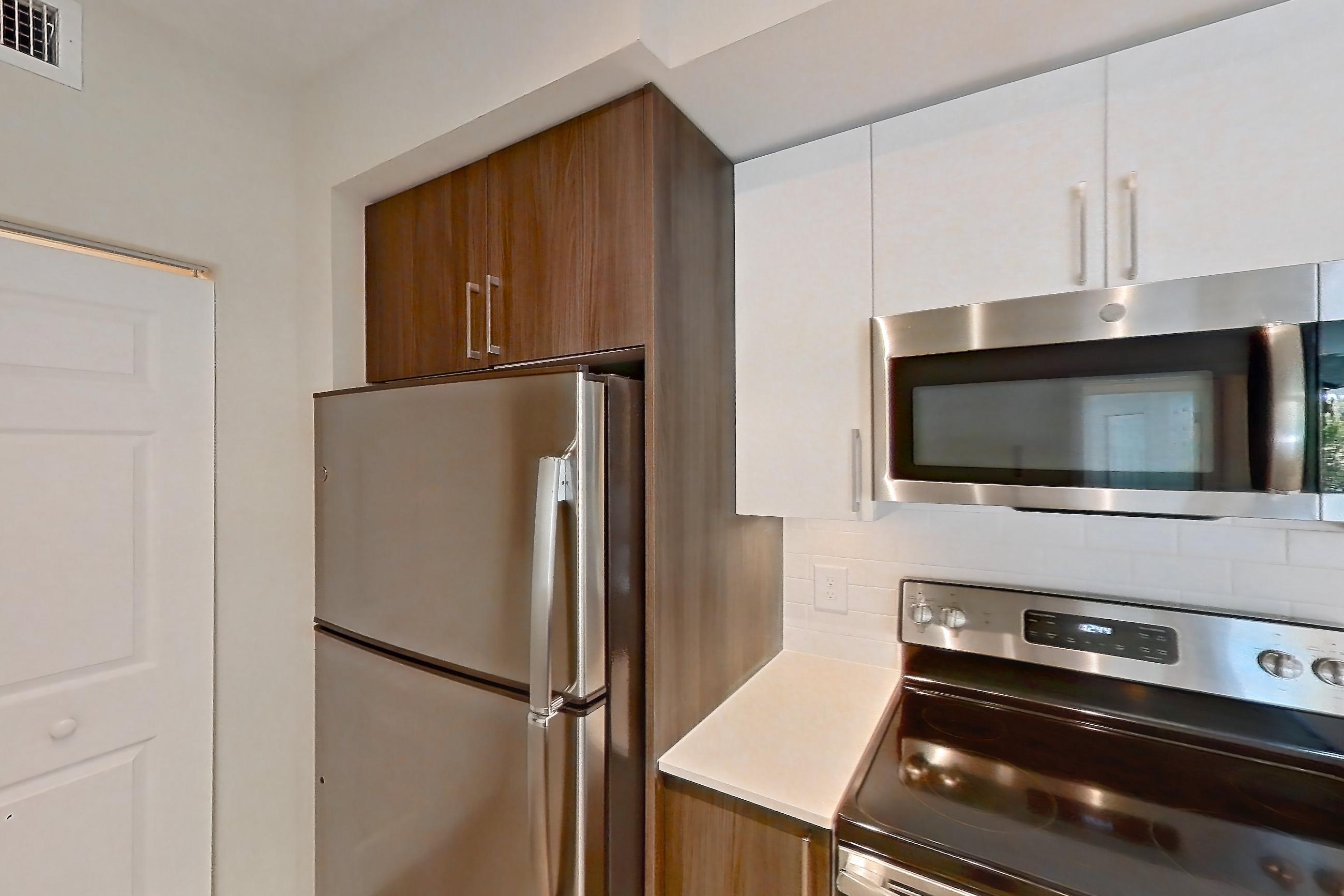 Kitchen with dishwasher, electric range, light countertops, light stone countertops, light wood-finish flooring, microwave, oven/range, refrigerator, and stainless steel appliances, Apartment 17-205 at Cortland South Kendall