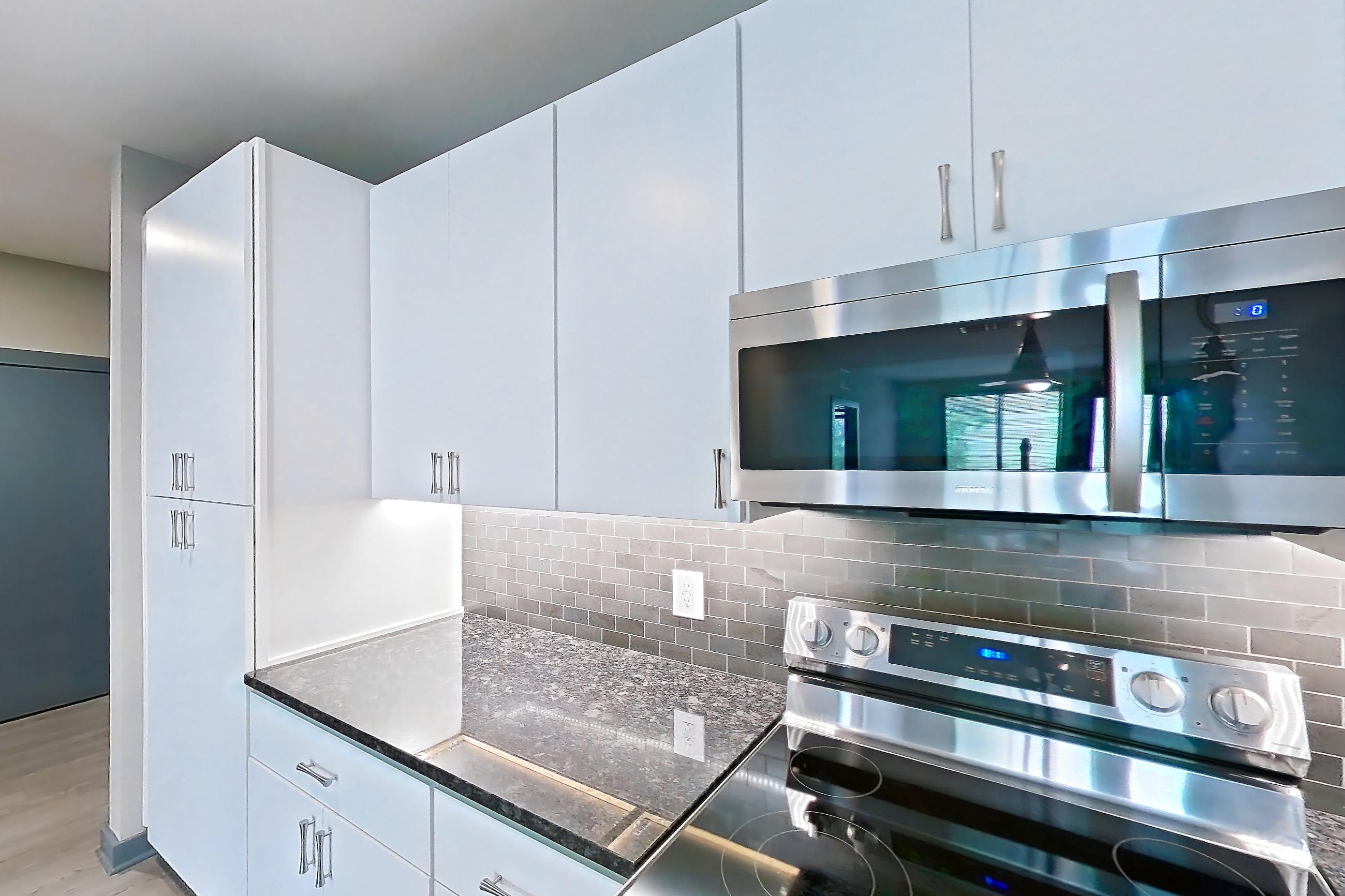 Kitchen with black appliances, dark stone countertops, dishwasher, electric range, kitchen island, light countertops, light wood-finish flooring, microwave, oven/range, refrigerator, and stainless steel appliances, Apartment 2040 at Cortland Westshore
